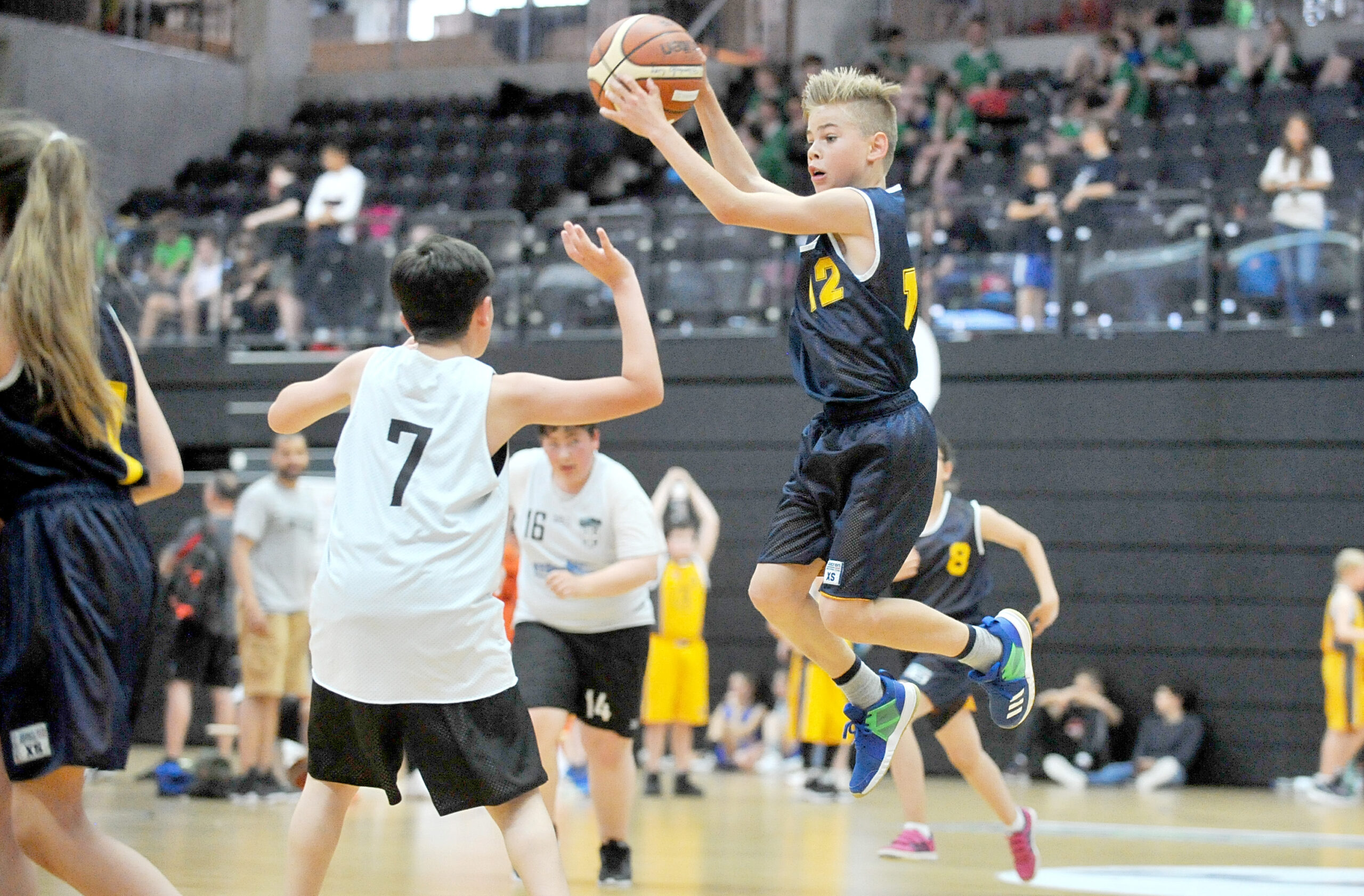 Junge Basketballspieler in Aktion, einer springt mit Ball zum Wurf, andere verteidigen auf dem Spielfeld