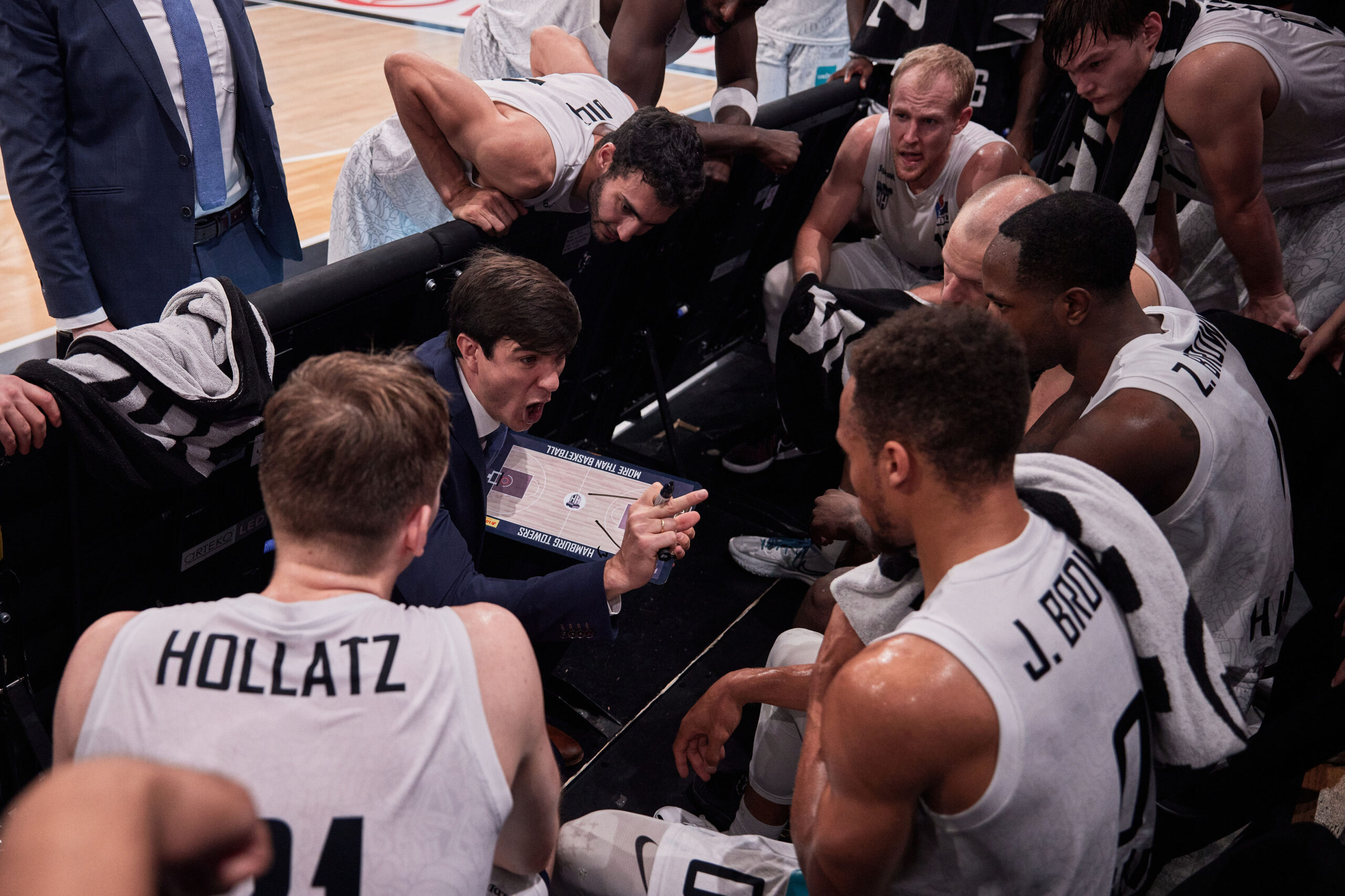 Basketballtrainer gibt seinem Team während einer Auszeit taktische Anweisungen, Spieler in weißen Trikots hören aufmerksam zu