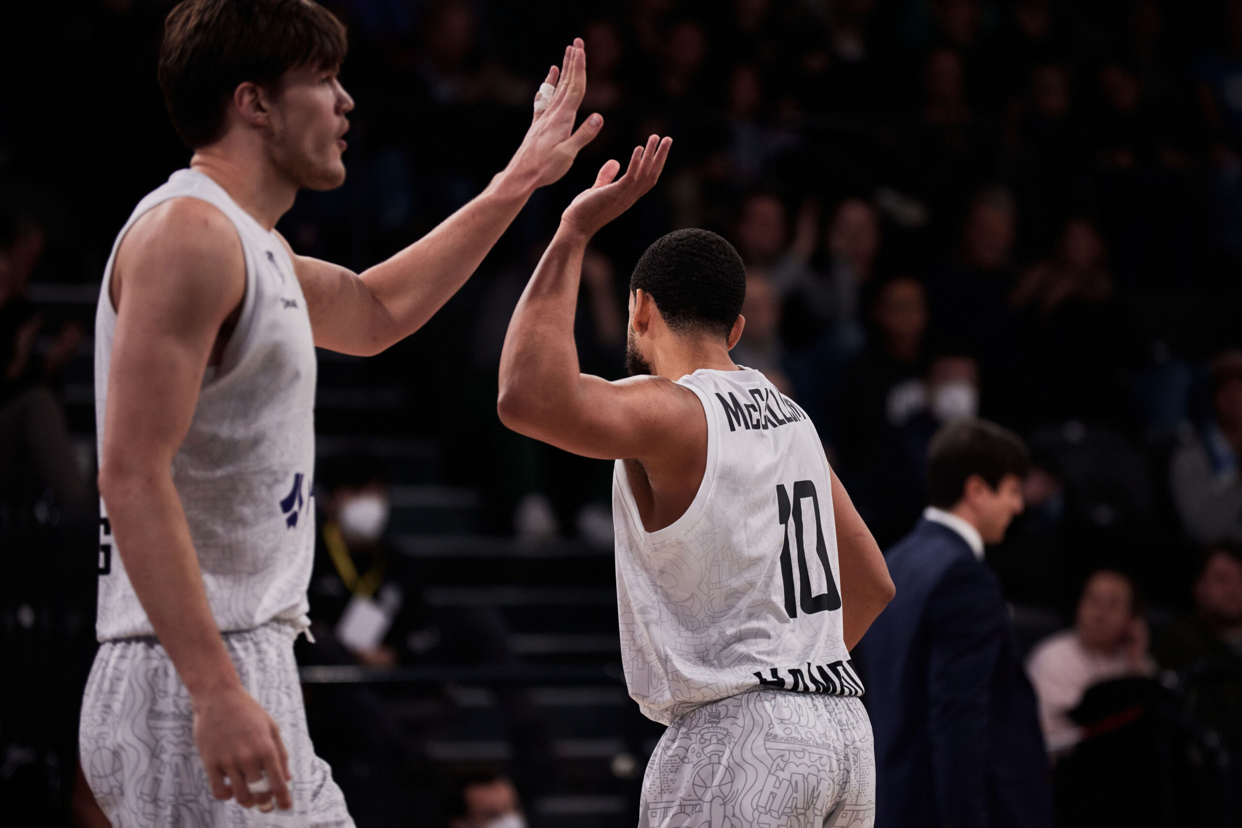 Zwei Basketballspieler in weißen Trikots geben sich während eines Spiels einen High-Five.