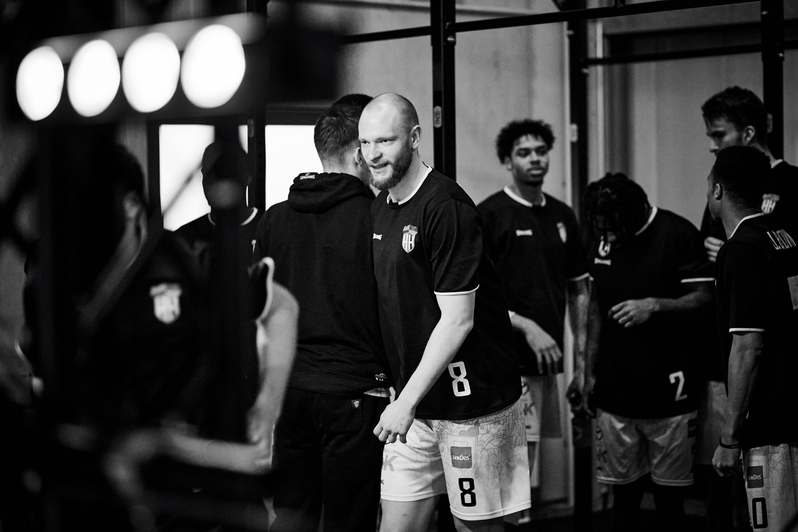Mann in Sporttrikot mit der Nummer 8 umarmt einen anderen Spieler, weitere Spieler im Hintergrund in einer Umkleidekabine