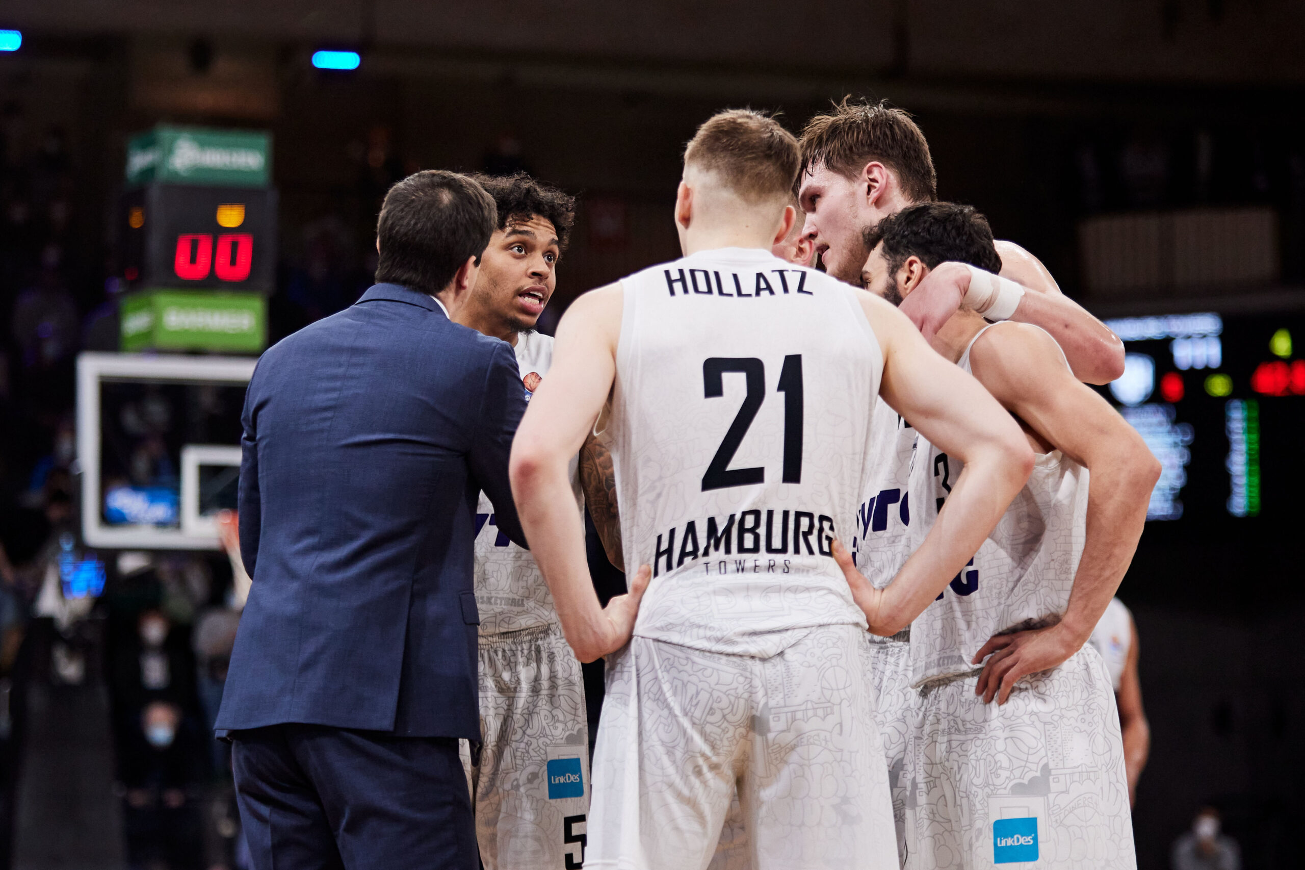 Basketballtrainer gibt Anweisungen an Spieler in weißen Trikots mit der Aufschrift 'Hamburg' während eines Spiels