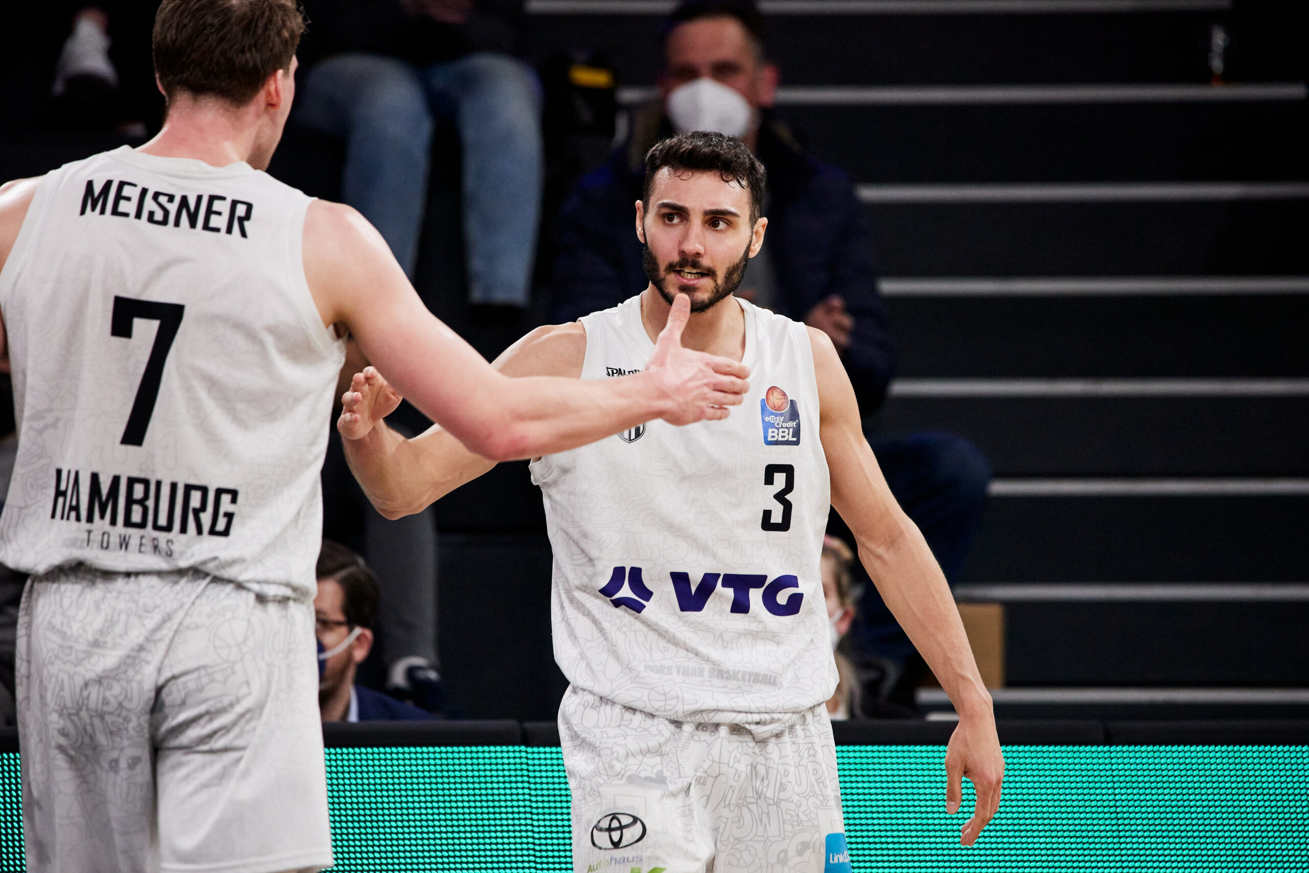 Zwei Basketballspieler der Hamburg Towers in weißen Trikots geben sich während eines Spiels einen Handschlag.
