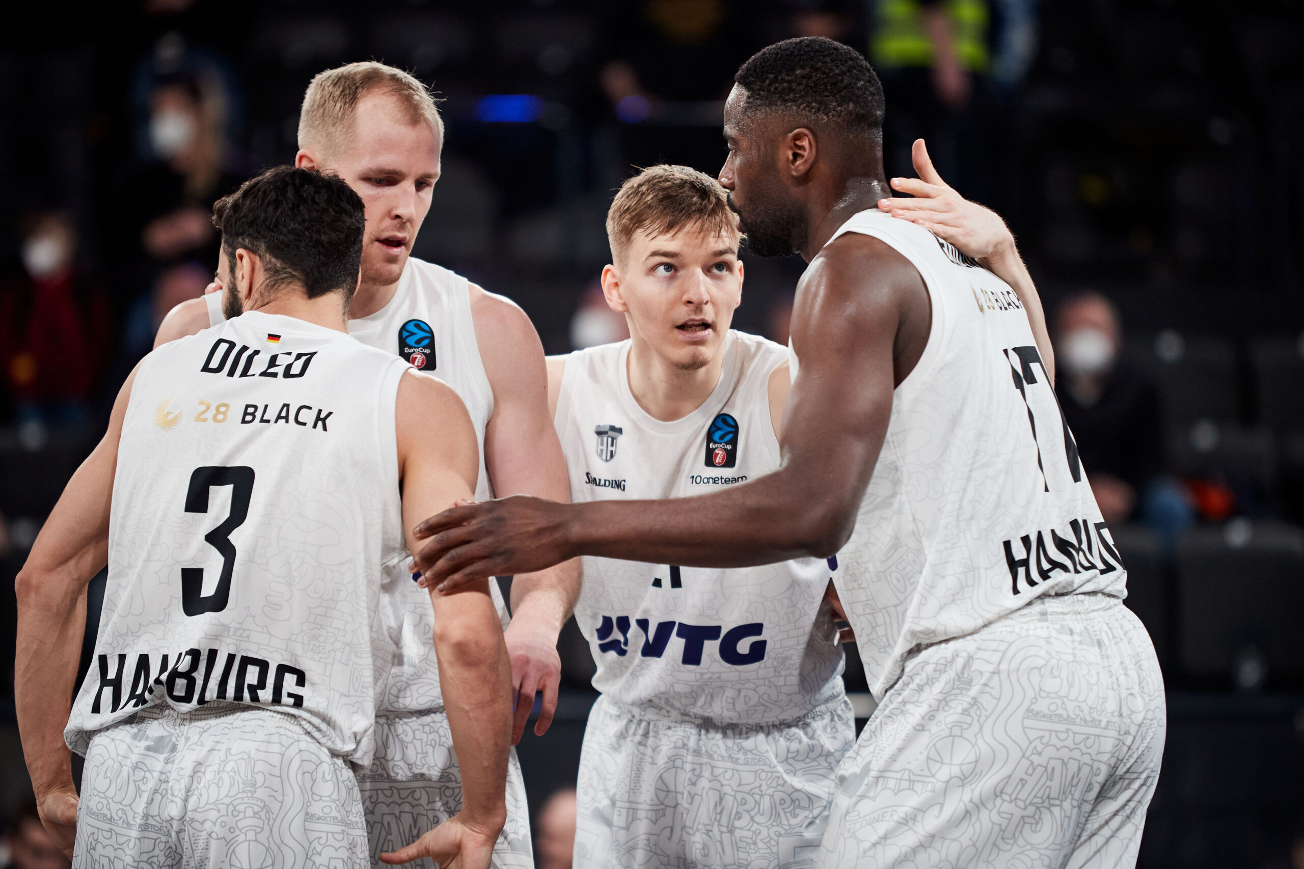 Vier Basketballspieler des Teams Hamburg in weißen Trikots diskutieren während eines Spiels