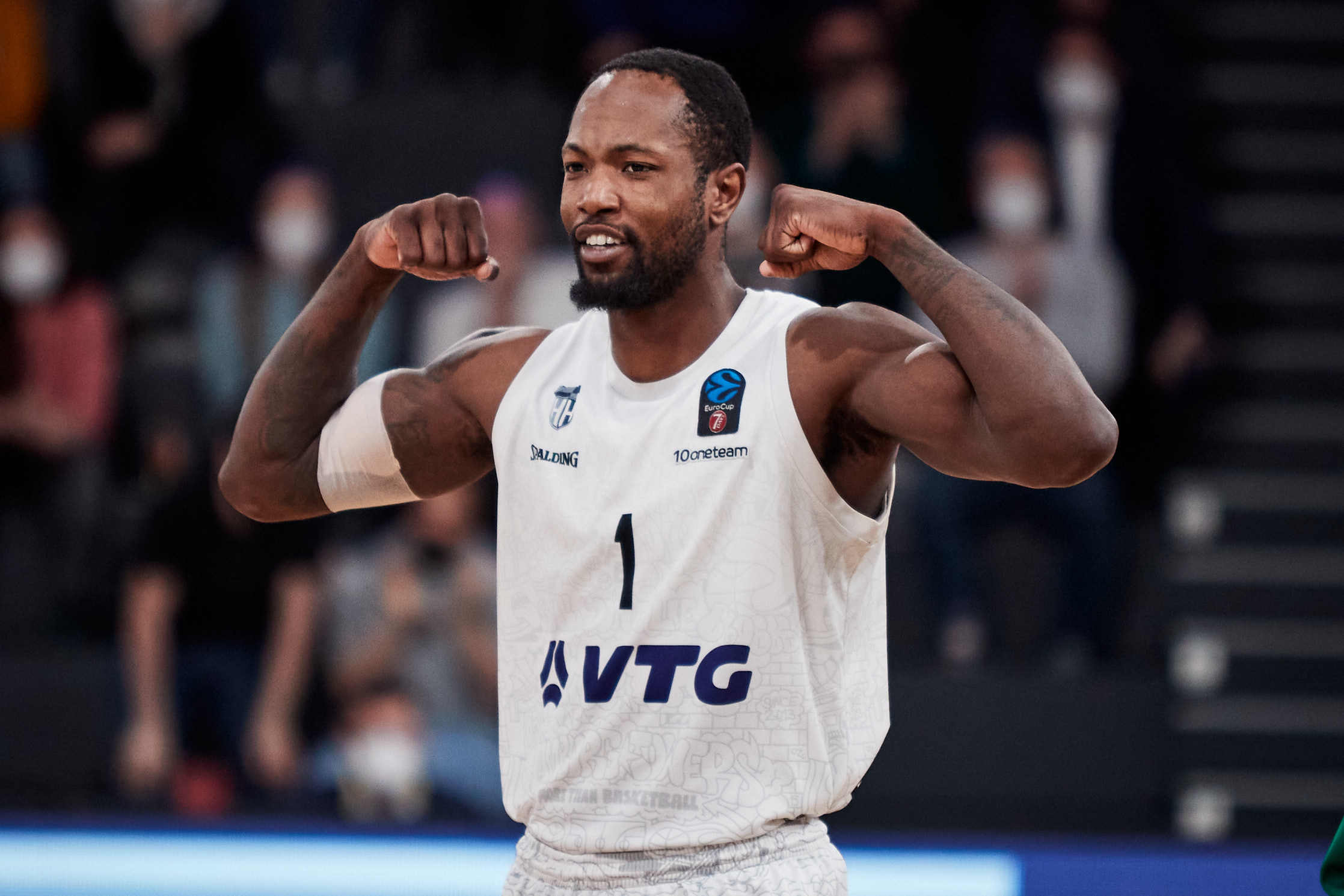 Basketballspieler in weißem Trikot mit der Nummer 1 zeigt muskulöse Arme und feiert