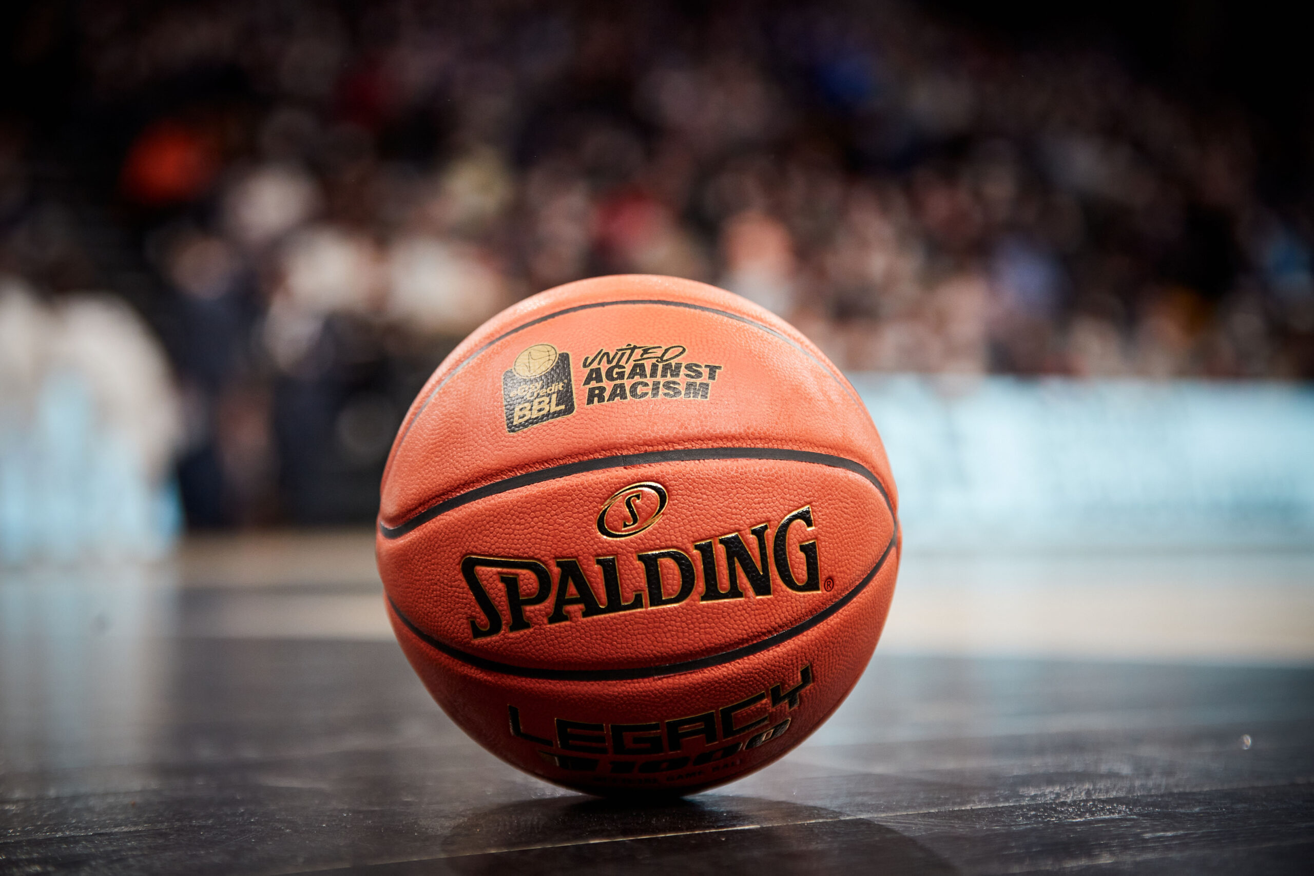 Oranger Basketball mit der Aufschrift 'Spalding' und 'United Against Racism' auf einem Hallenboden