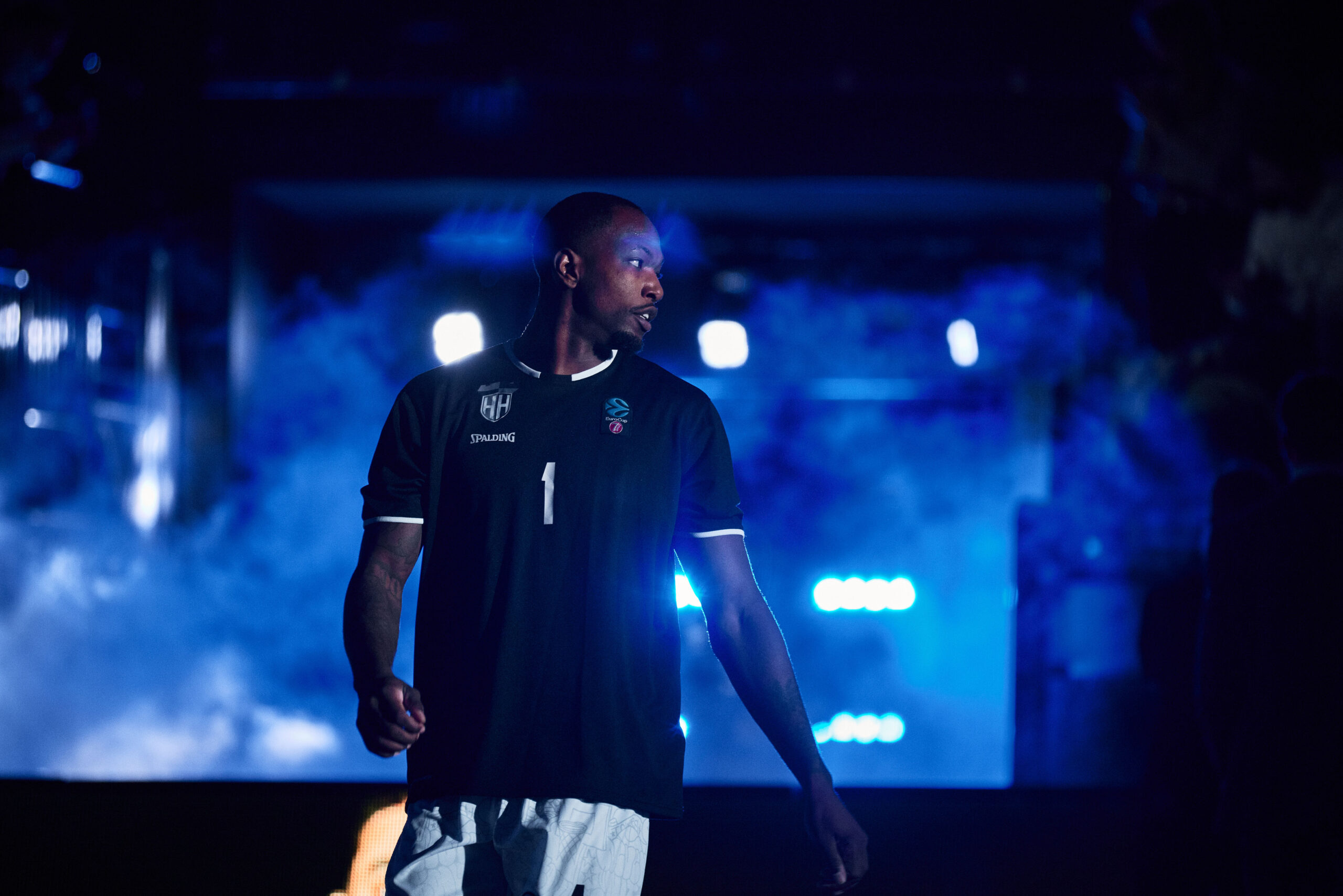 Basketballspieler in schwarzem Trikot mit der Nummer 1 vor blau beleuchtetem Hintergrund