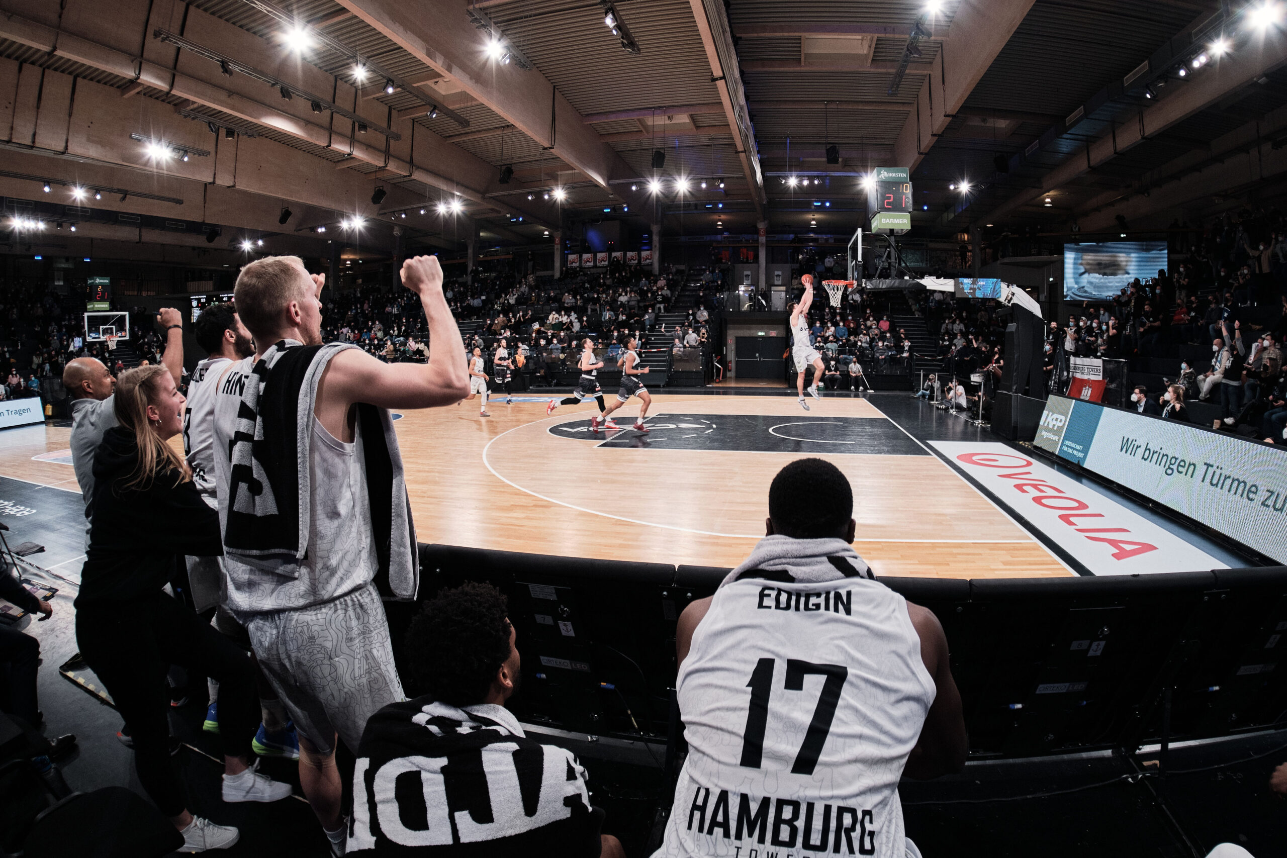 Basketballspieler und Zuschauer auf der Bank jubeln während eines Spiels in einer Halle mit vielen Zuschauern