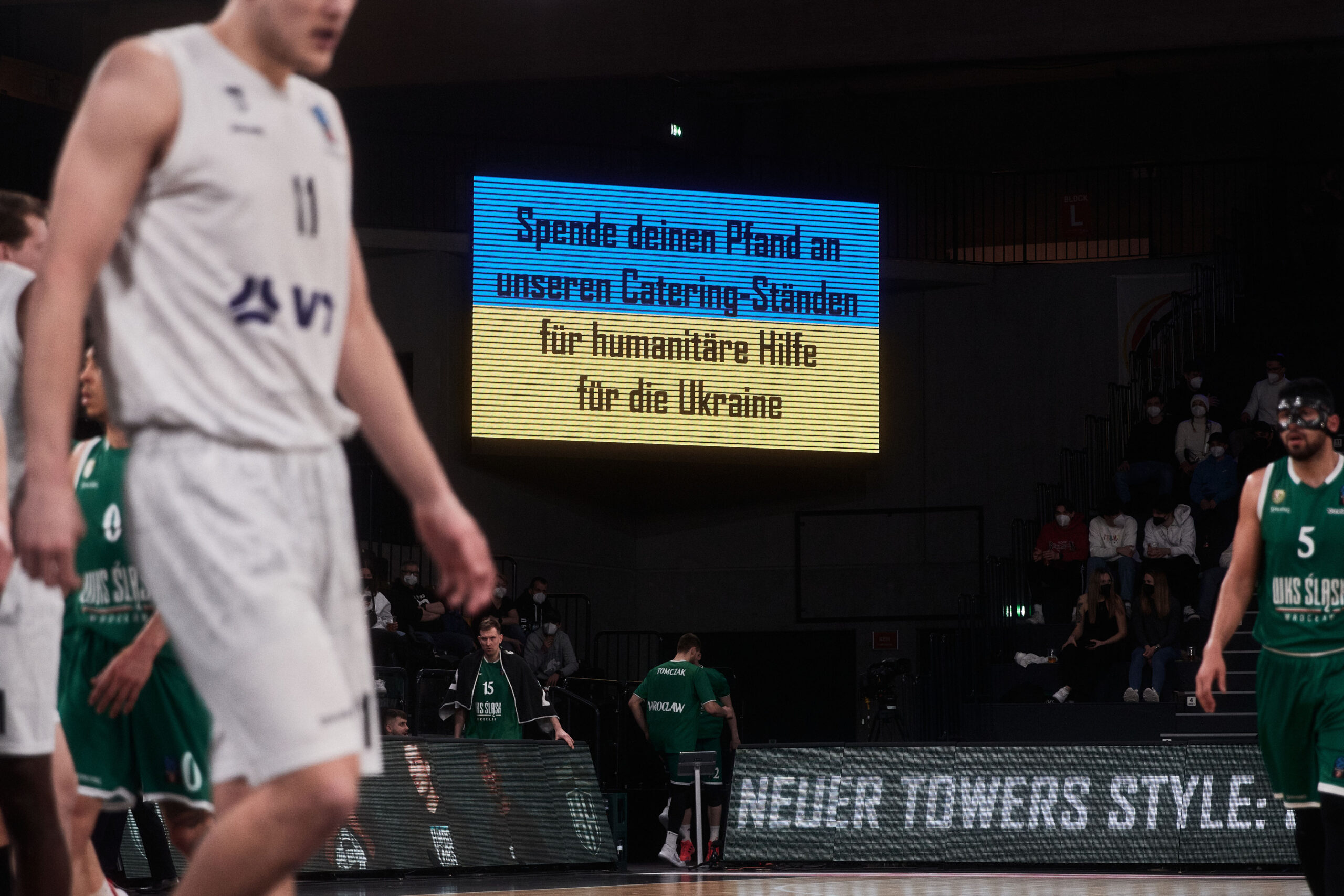 Leuchttafel mit Text 'Spende deinen Pfand an unseren Catering-Ständen für humanitäre Hilfe für die Ukraine' bei einem Basketballspiel