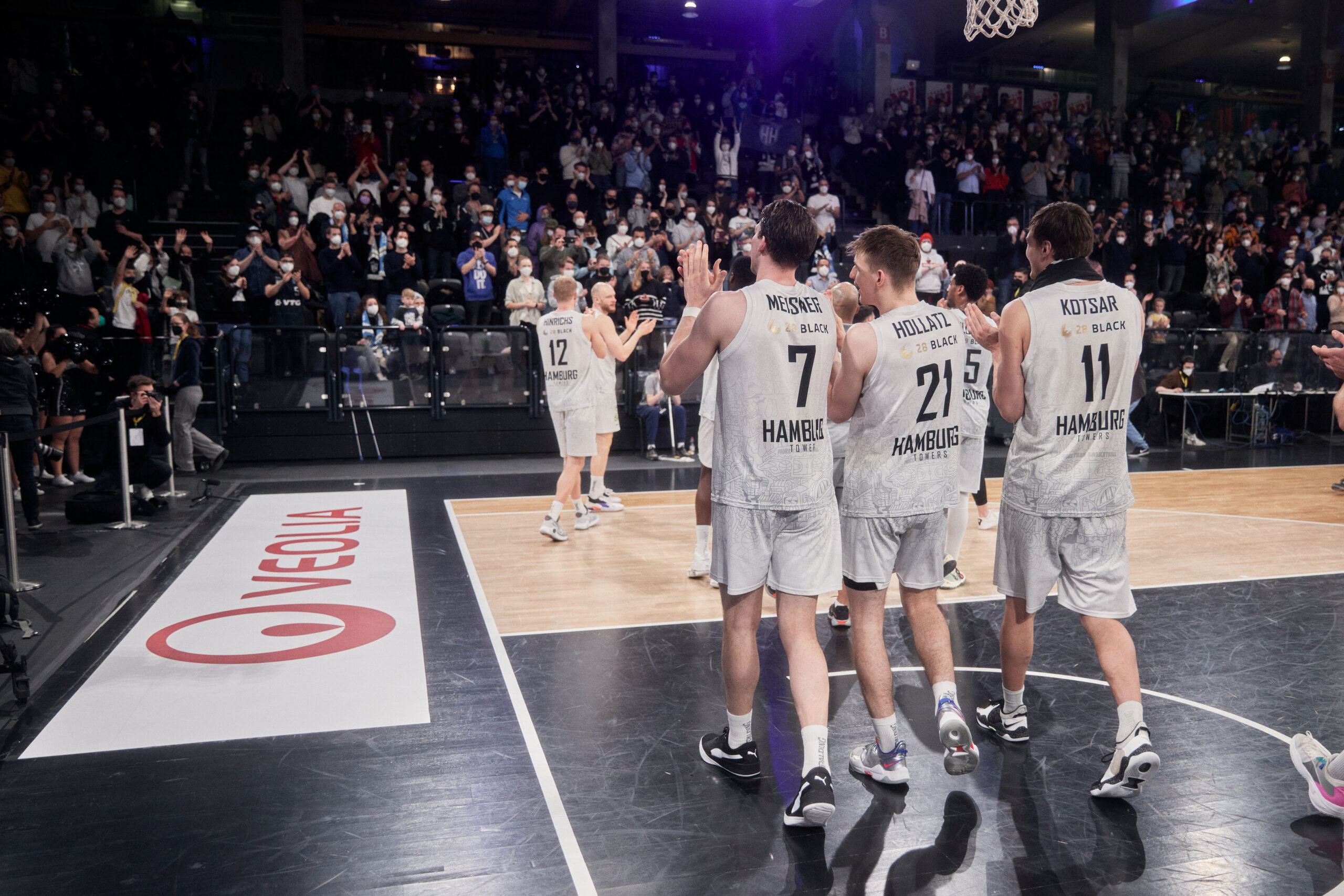 Basketballspieler der Hamburg Towers in weißen Trikots verlassen das Spielfeld, Zuschauer applaudieren im Hintergrund