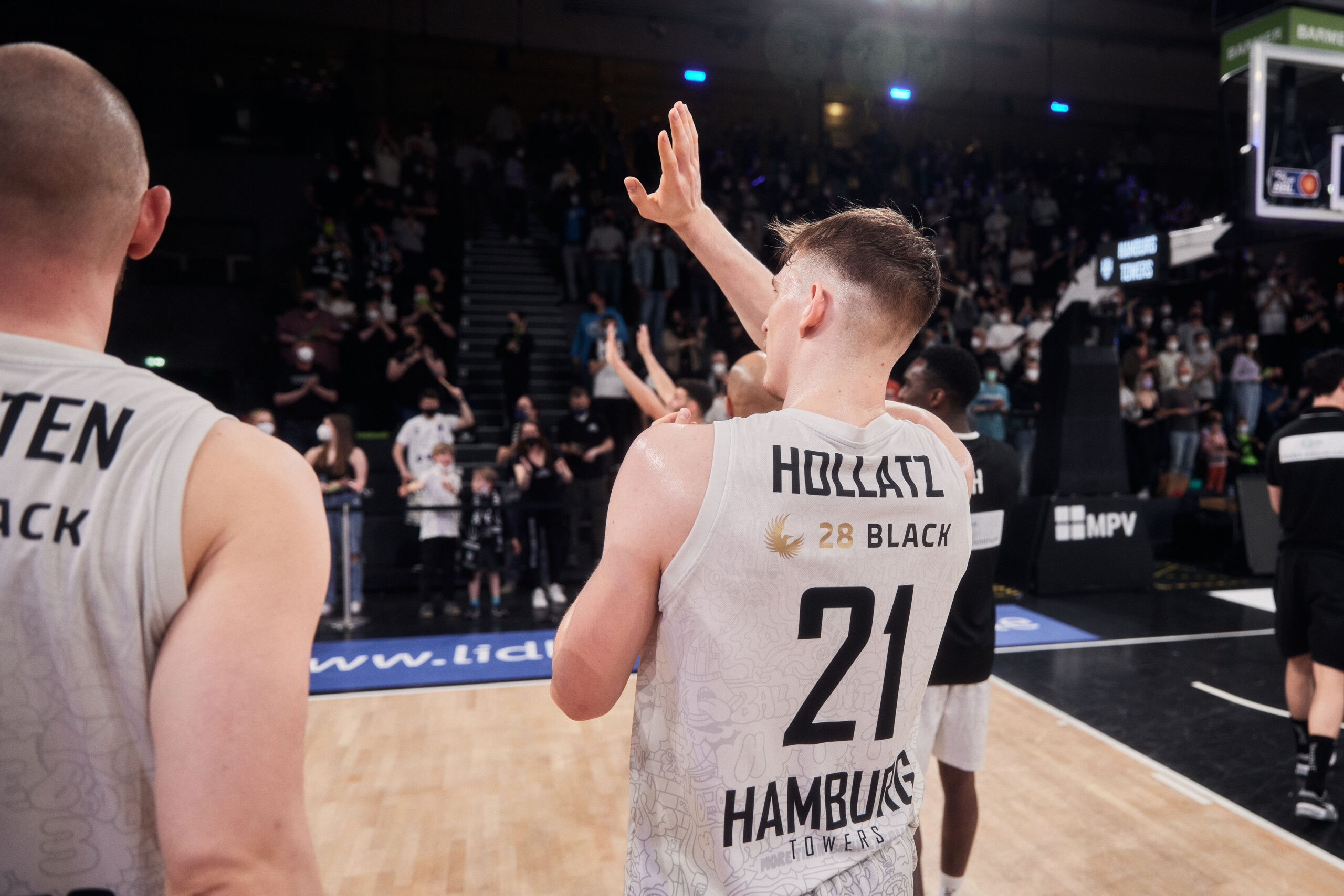 Basketballspieler mit Trikotnummer 21 und Aufschrift 'Hamburg Towers' winkt zum Publikum in einer Halle