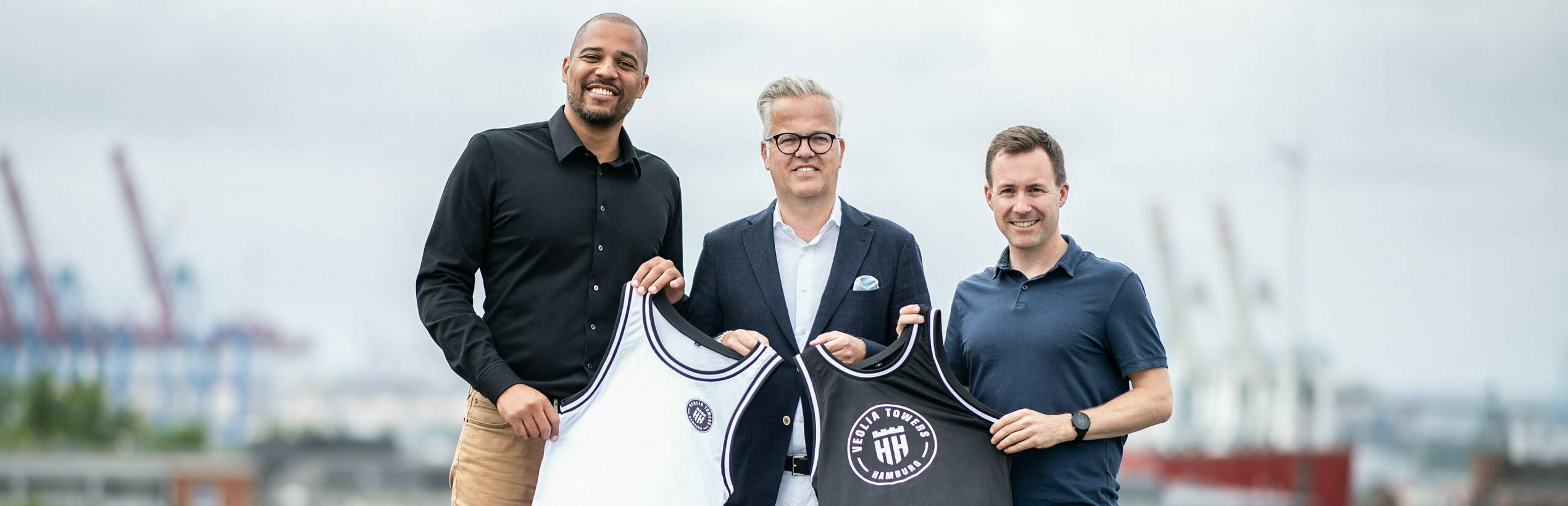 Marvin Willoughby, Matthias Harms von Veolia und Jan Fischer mit Trikot vor Hafenpanorama