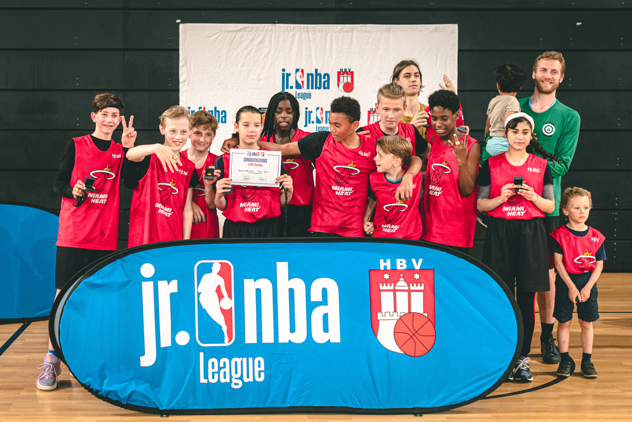 Kinder in roten Trikots posieren hinter einem Werbebanner mit der Aufschrift "Jr. NBA"