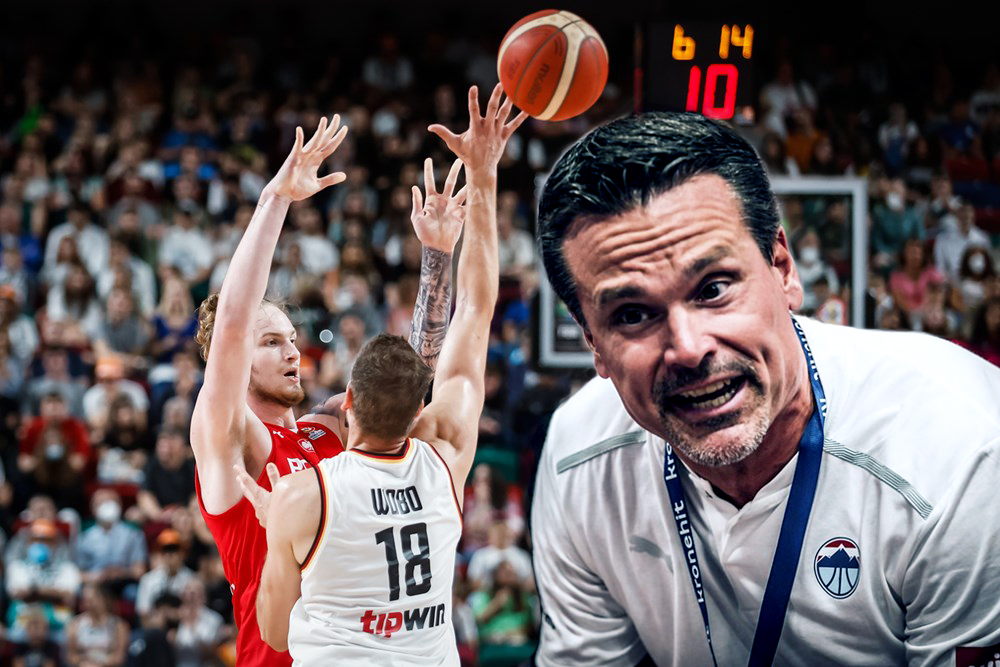 Basketballspiel mit zwei Spielern in Aktion, einer wirft den Ball, im Vordergrund ein Trainer mit konzentriertem Gesichtsausdruck und Trikot mit Logo