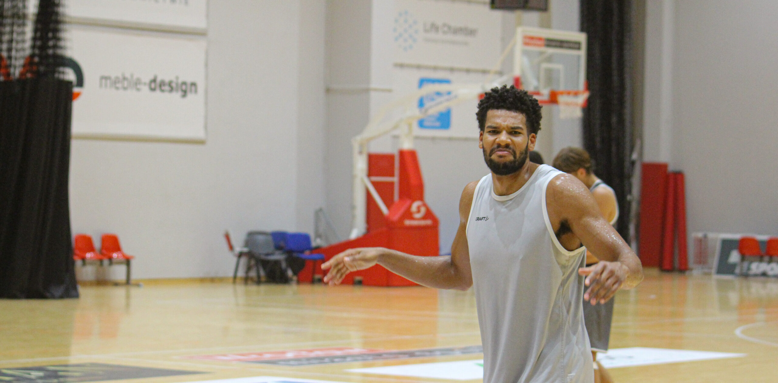 Basketballspieler in grauem Trikot auf einem Hallenbasketballfeld, der die Arme ausbreitet