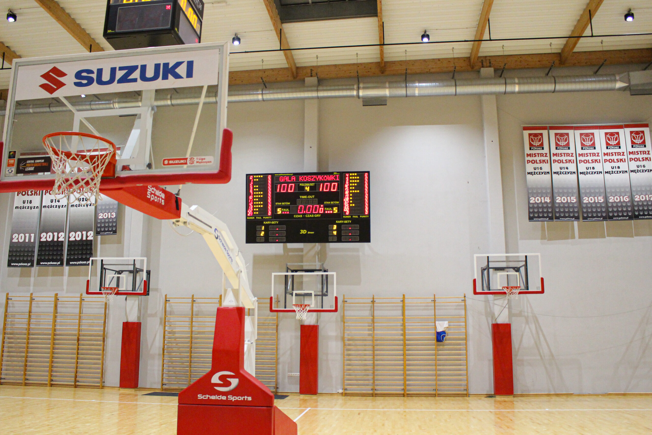 Leere Basketballhalle mit drei Körben, Anzeigetafel zeigt 100 zu 100 und 0:00 Spielzeit, Suzuki-Werbung am Korb
