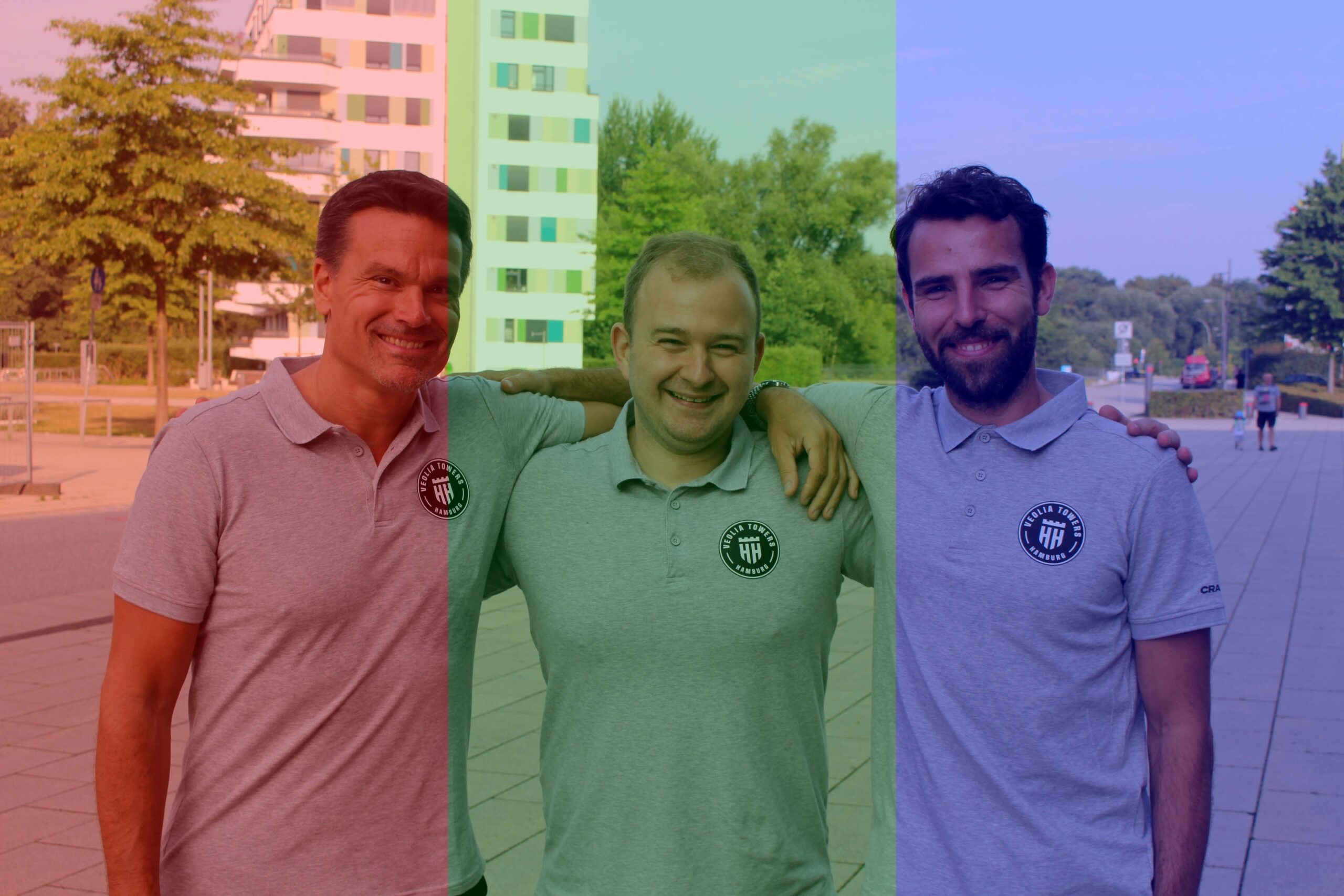 Drei Männer in grauen Poloshirts mit Logo, die draußen vor Gebäuden und Bäumen stehen, lächelnd und mit Armen umeinander.