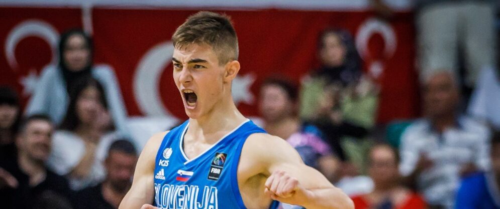 Junger Basketballspieler in blauem Trikot mit Aufschrift 'SLOVENIJA' jubelt mit geöffnetem Mund und angespannten Armen während eines Spiels