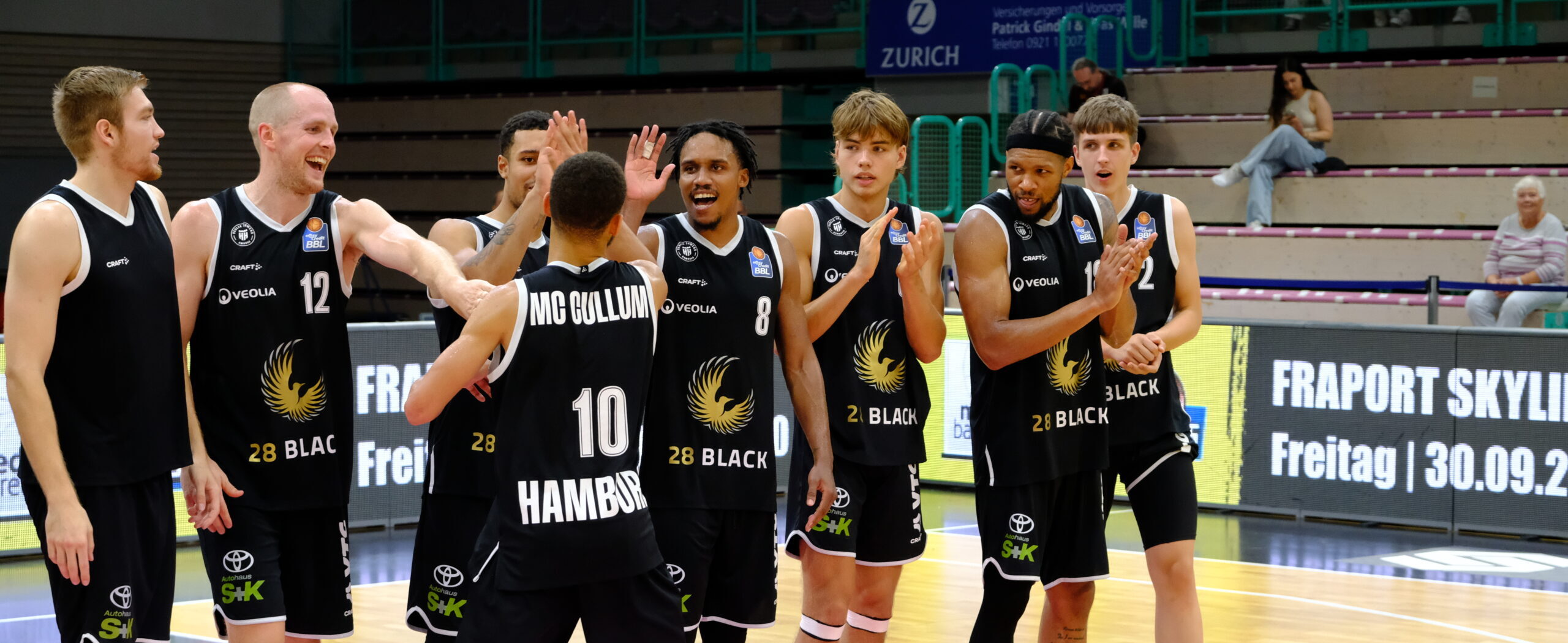 Basketballspieler in schwarzen Trikots mit der Aufschrift '28 Black' und 'Hamburg' klatschen sich auf dem Spielfeld ab