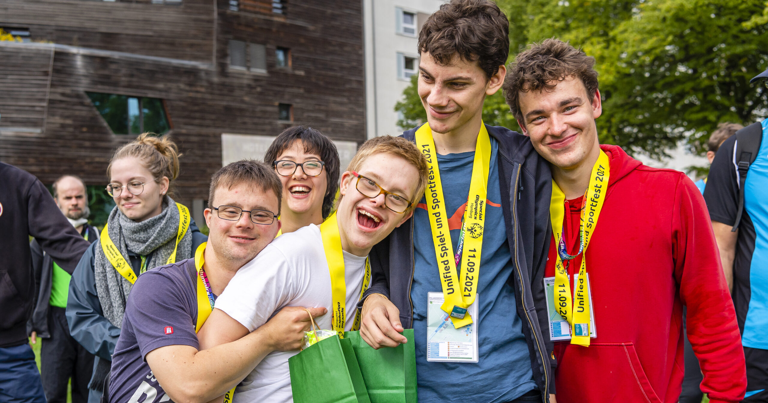 Gruppe lachender junger Menschen mit gelben Medaillenbändern bei einem Sportfest im Freien