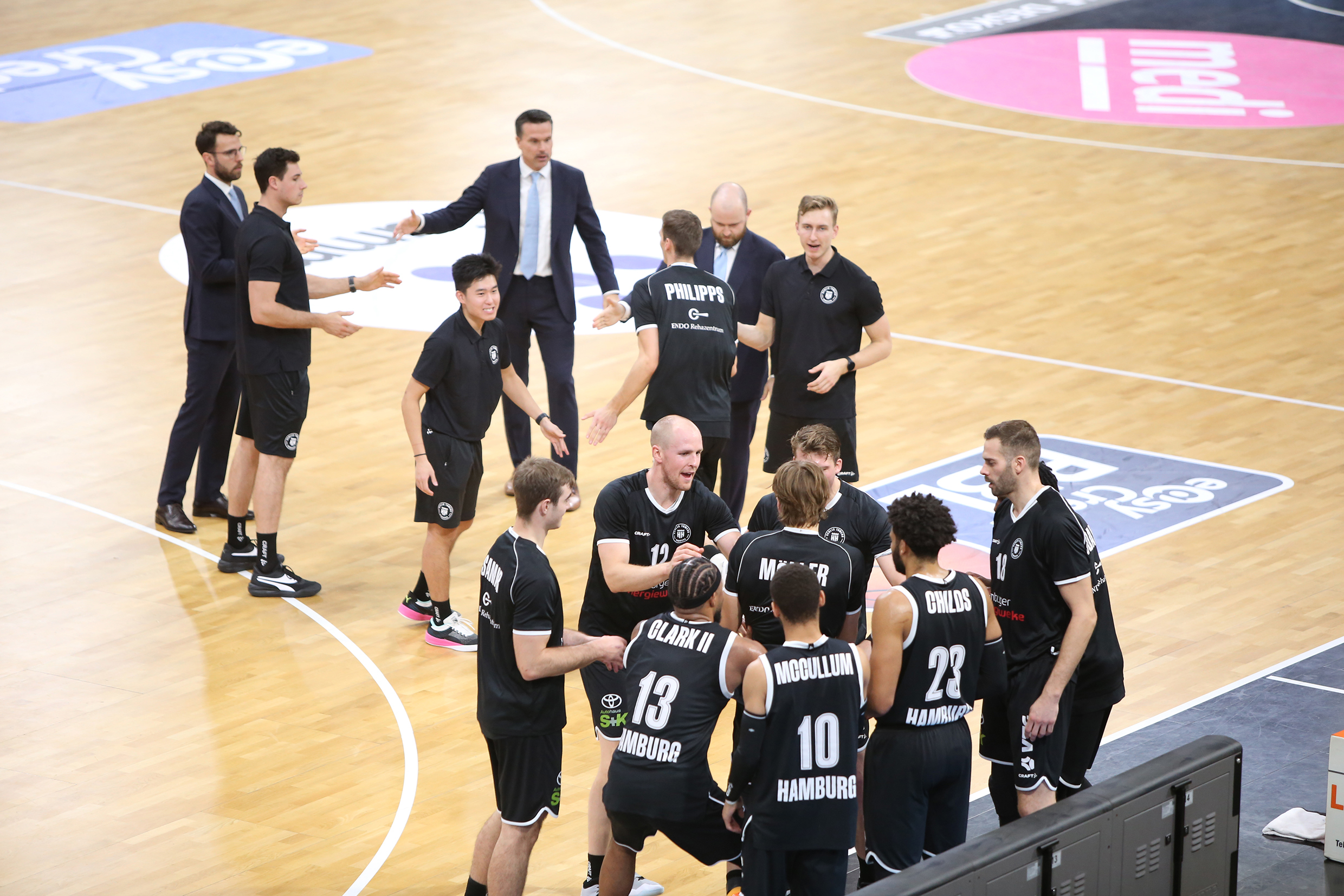 Basketballspieler und Trainer in schwarzen Trikots und Anzügen auf dem Spielfeld während einer Teambesprechung