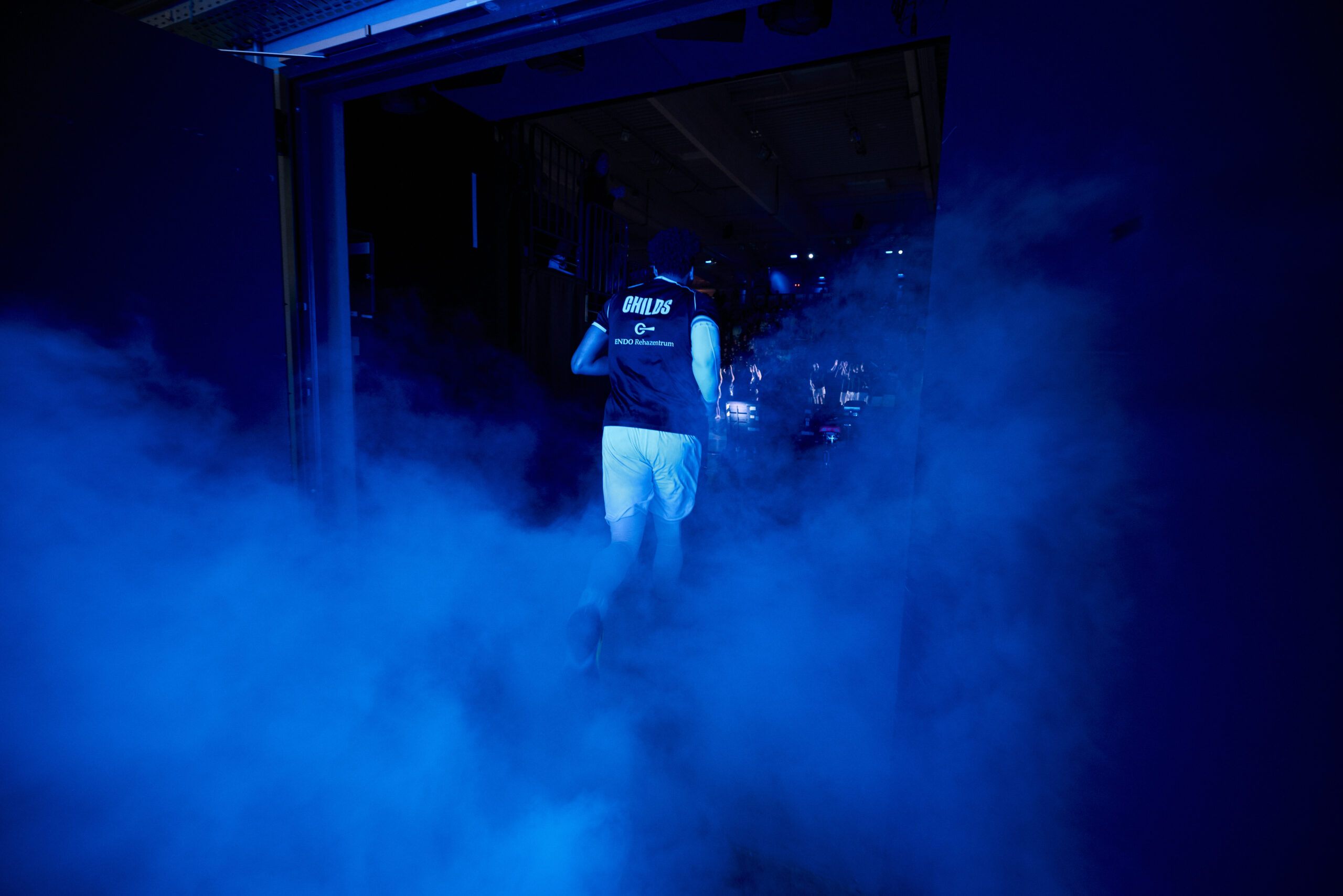 Basketballspieler läuft durch Nebel in eine dunkle Halle, trägt Trikot mit der Aufschrift 'TOWERS'
