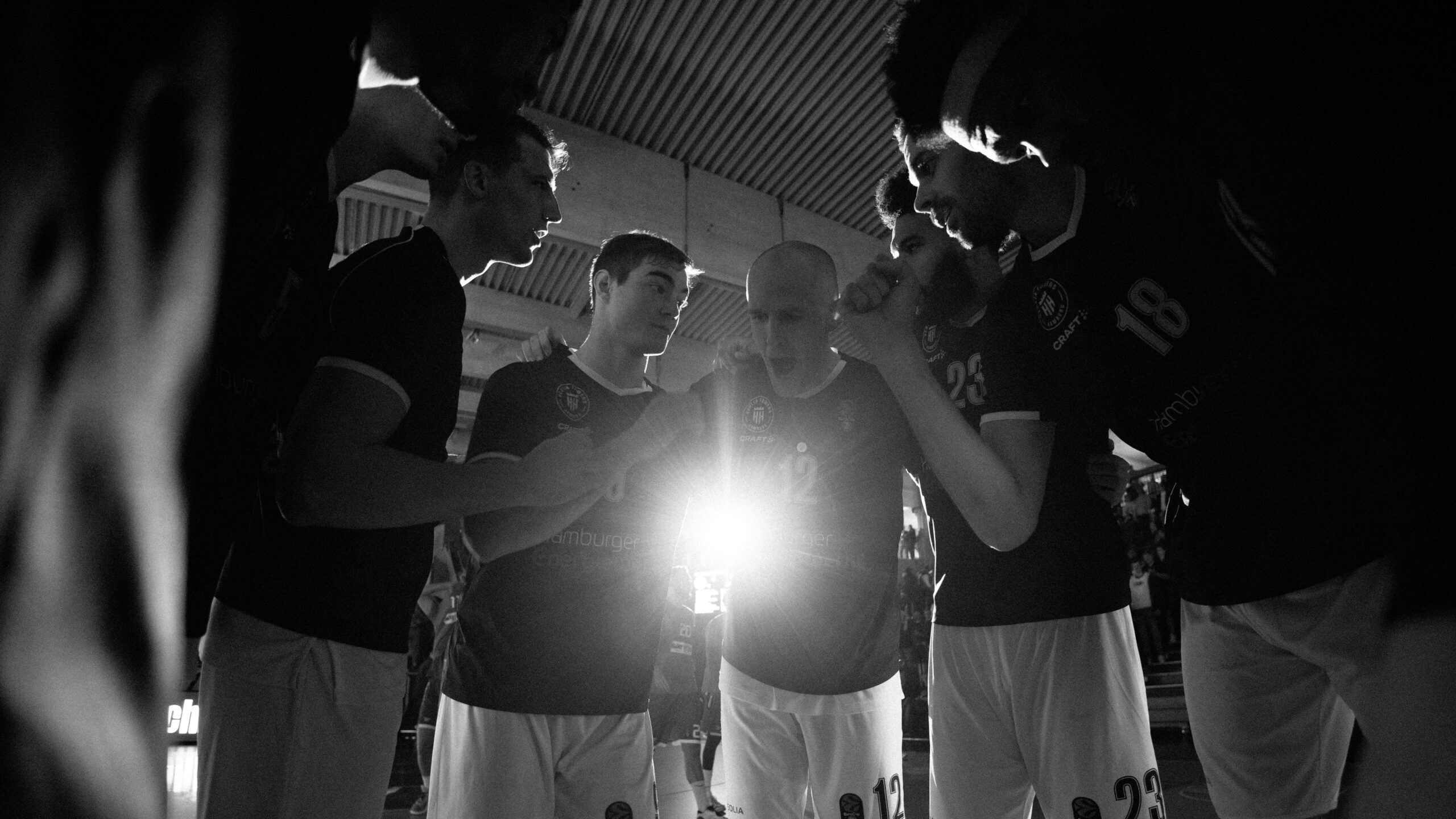 Basketballspieler in dunklen Trikots stehen im Kreis und besprechen sich während eines Spiels