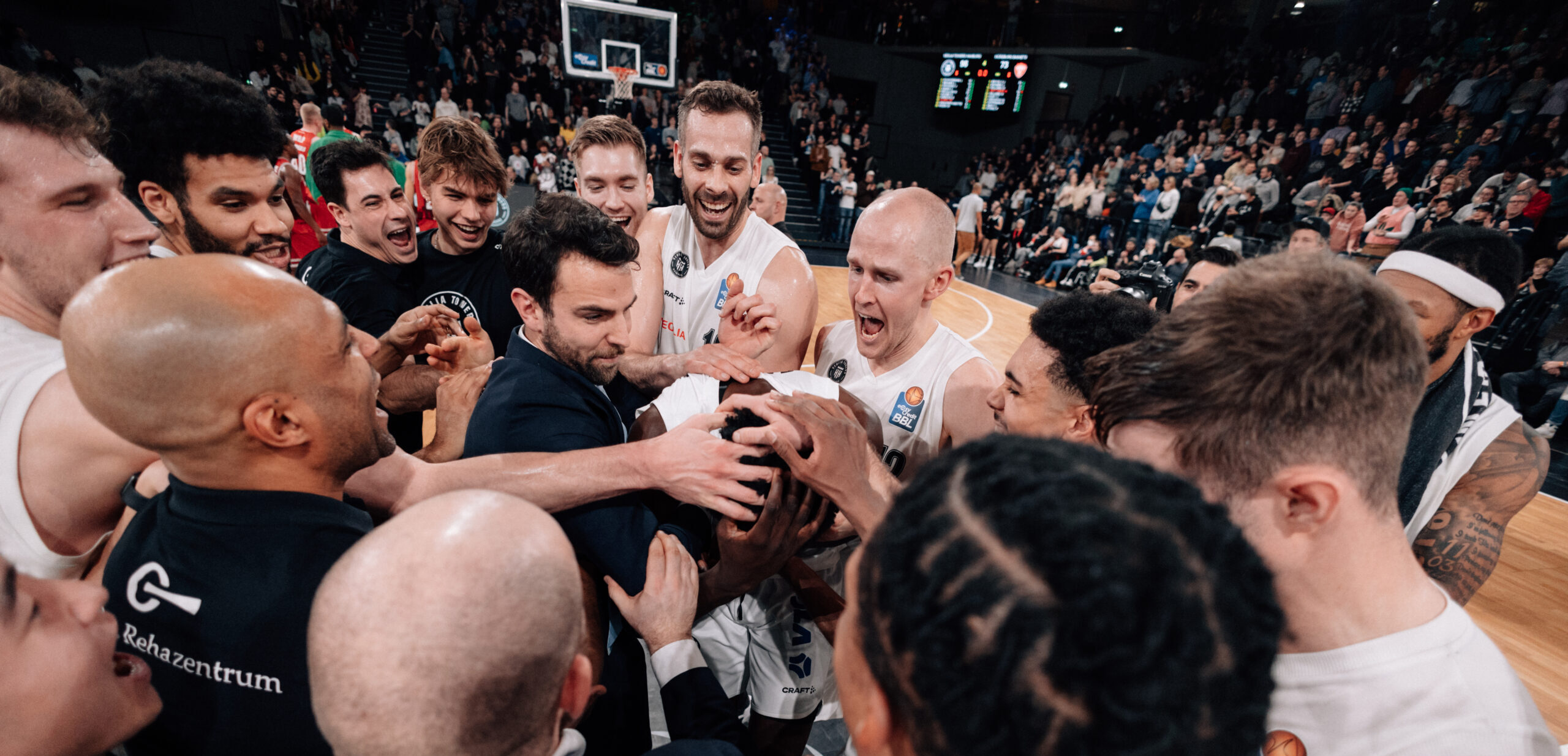 Basketballspieler und Teammitglieder feiern jubelnd auf dem Spielfeld nach einem Spiel