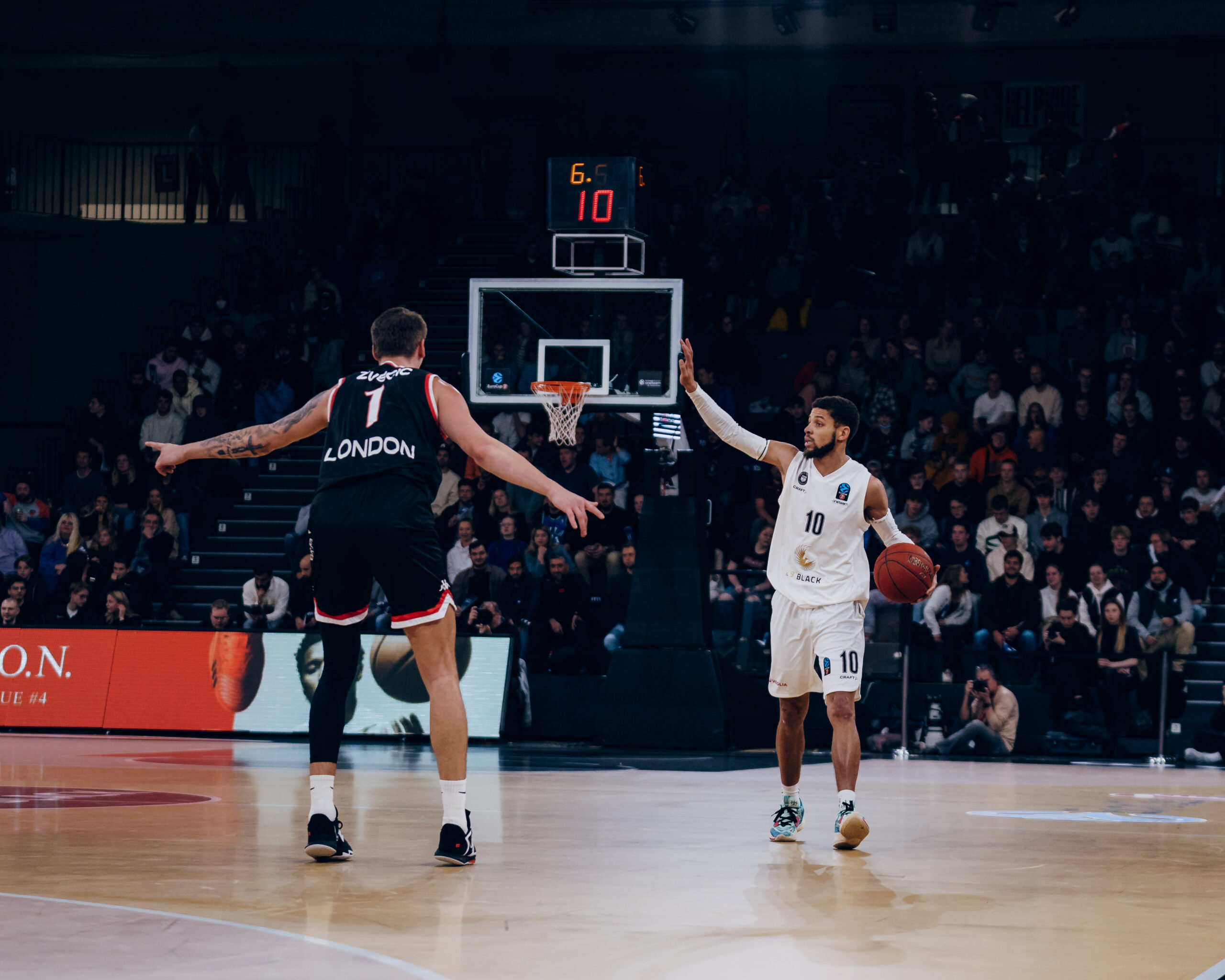 Zwei Basketballspieler auf dem Spielfeld, einer in weißer und einer in schwarzer Trikotfarbe, verteidigt gegen den anderen mit Ball in der Hand