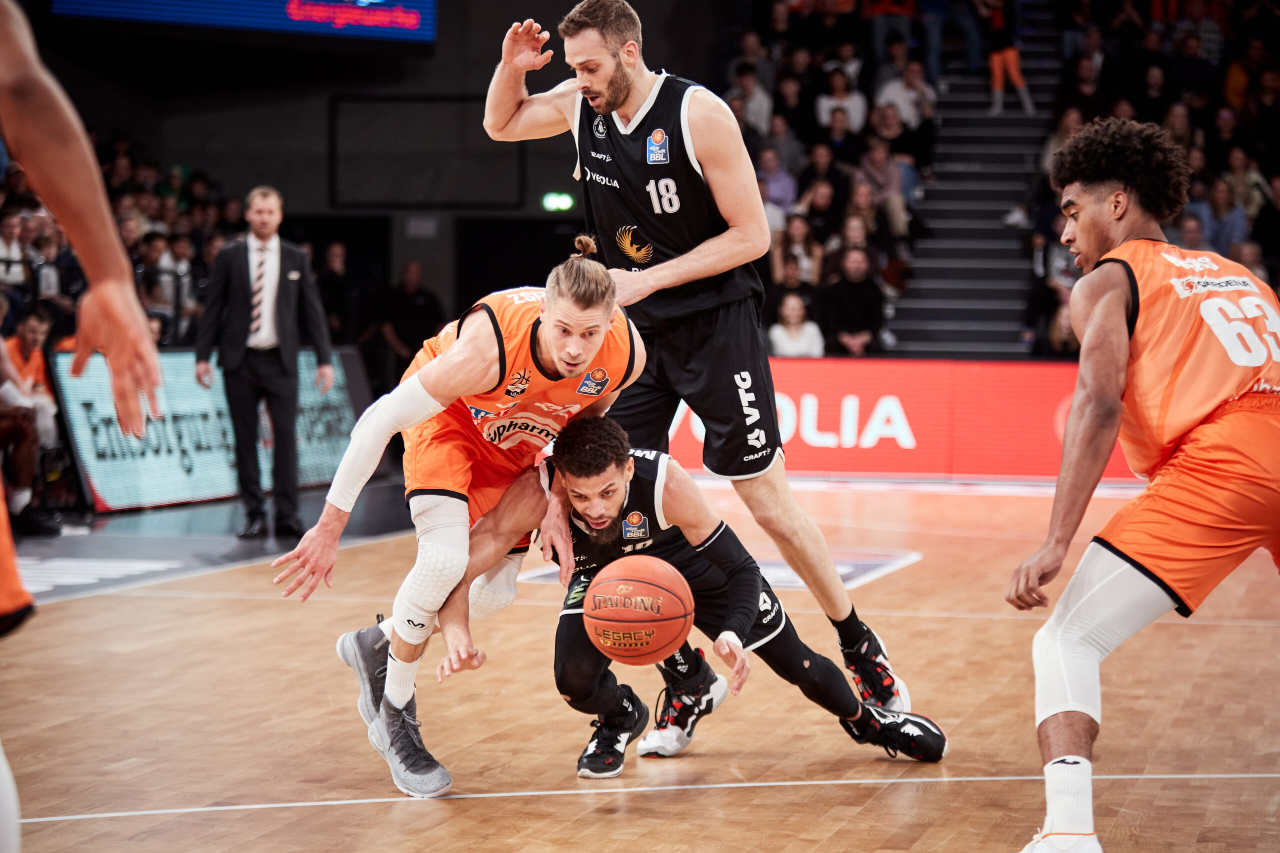 Basketballspiel zwischen zwei Teams, Spieler in orange und schwarz kämpfen um den Ball auf dem Spielfeld