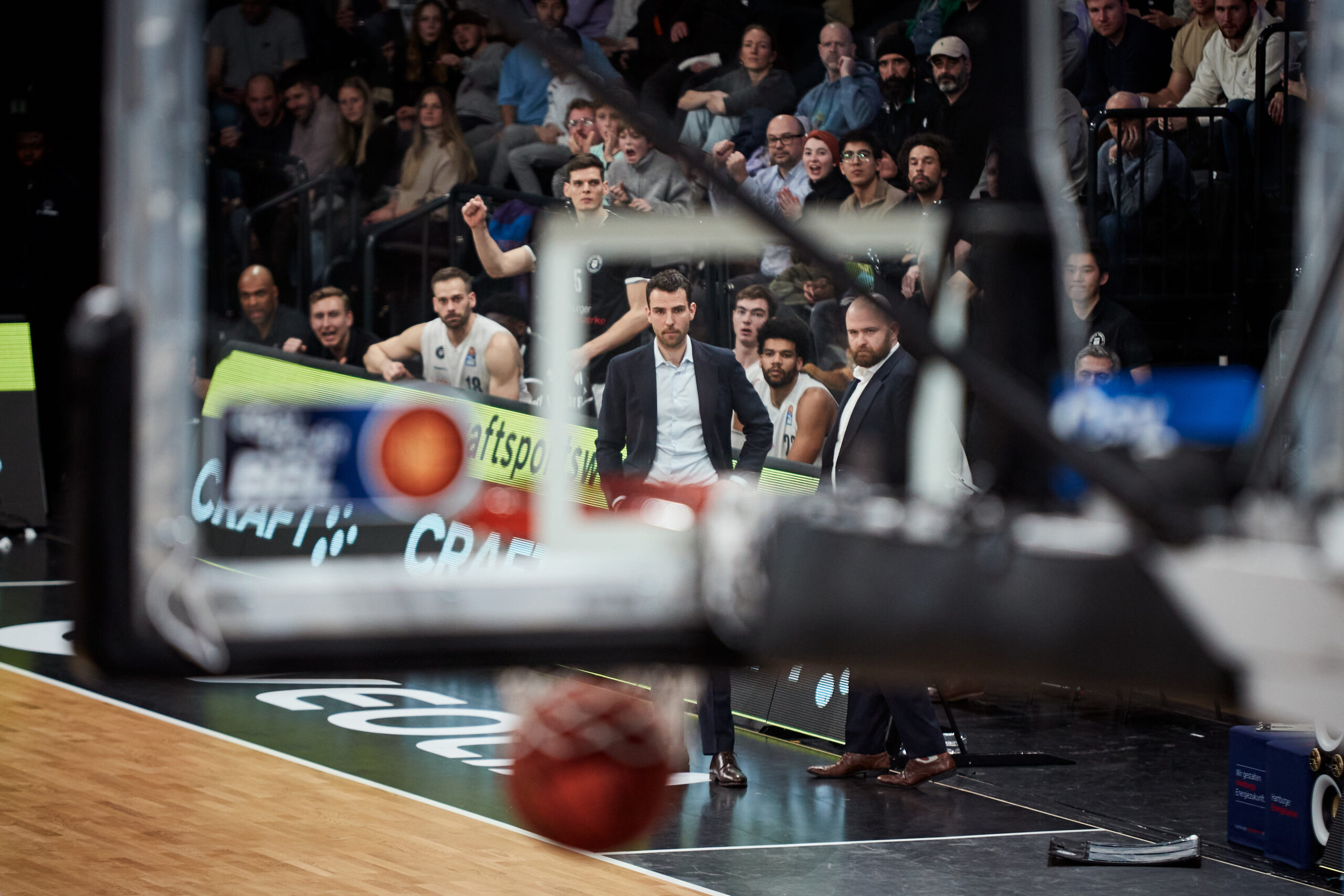 Basketballspieler wirft Ball zum Korb während eines Spiels vor Zuschauern auf der Tribüne