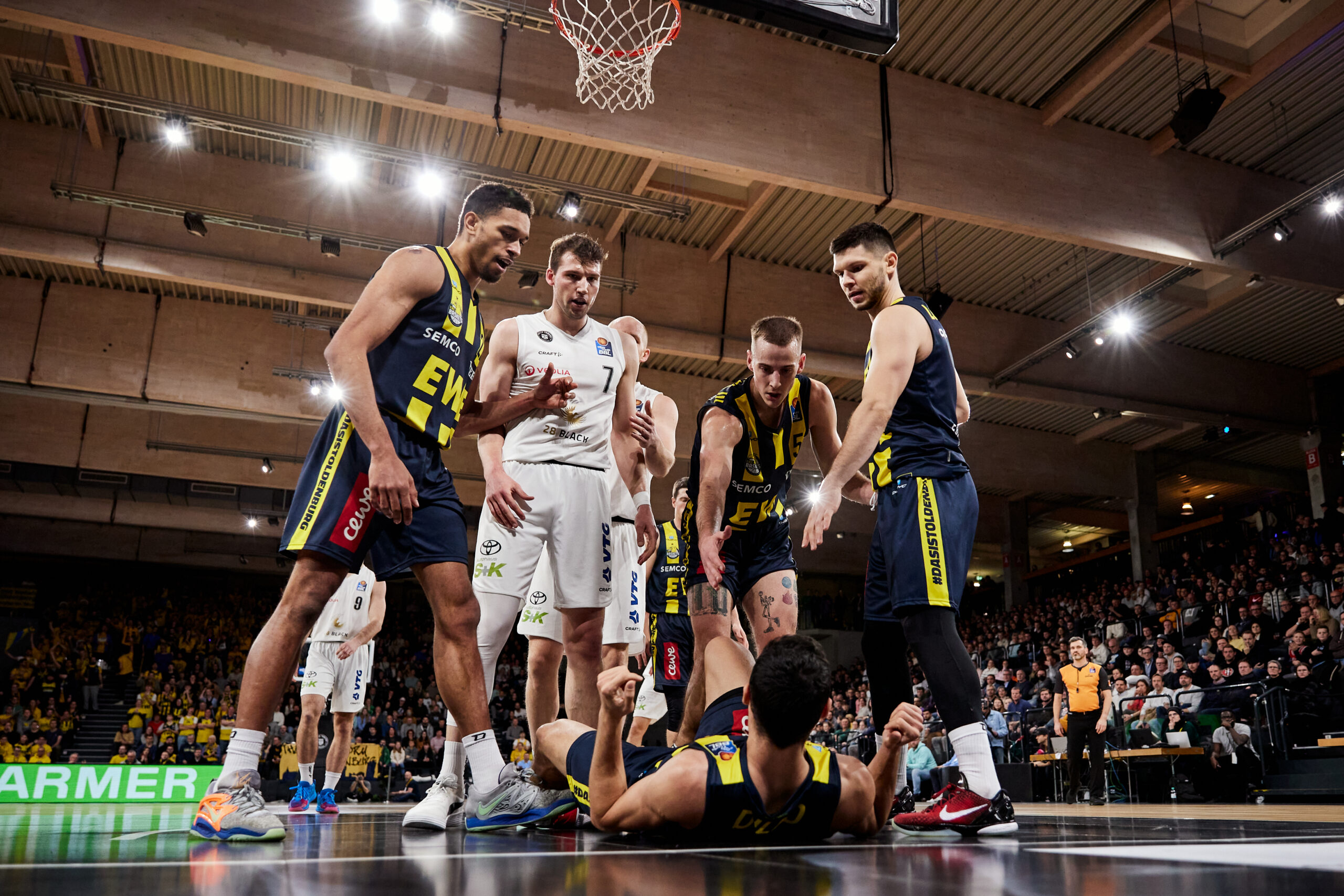 Fünf Basketballspieler in Aktion unter dem Korb während eines Spiels, Zuschauer im Hintergrund