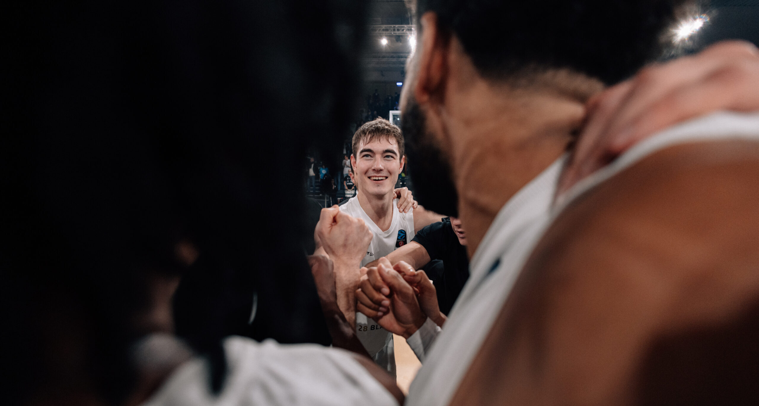 Basketballspieler in weißen Trikots umarmen sich während eines Spiels in einer Halle