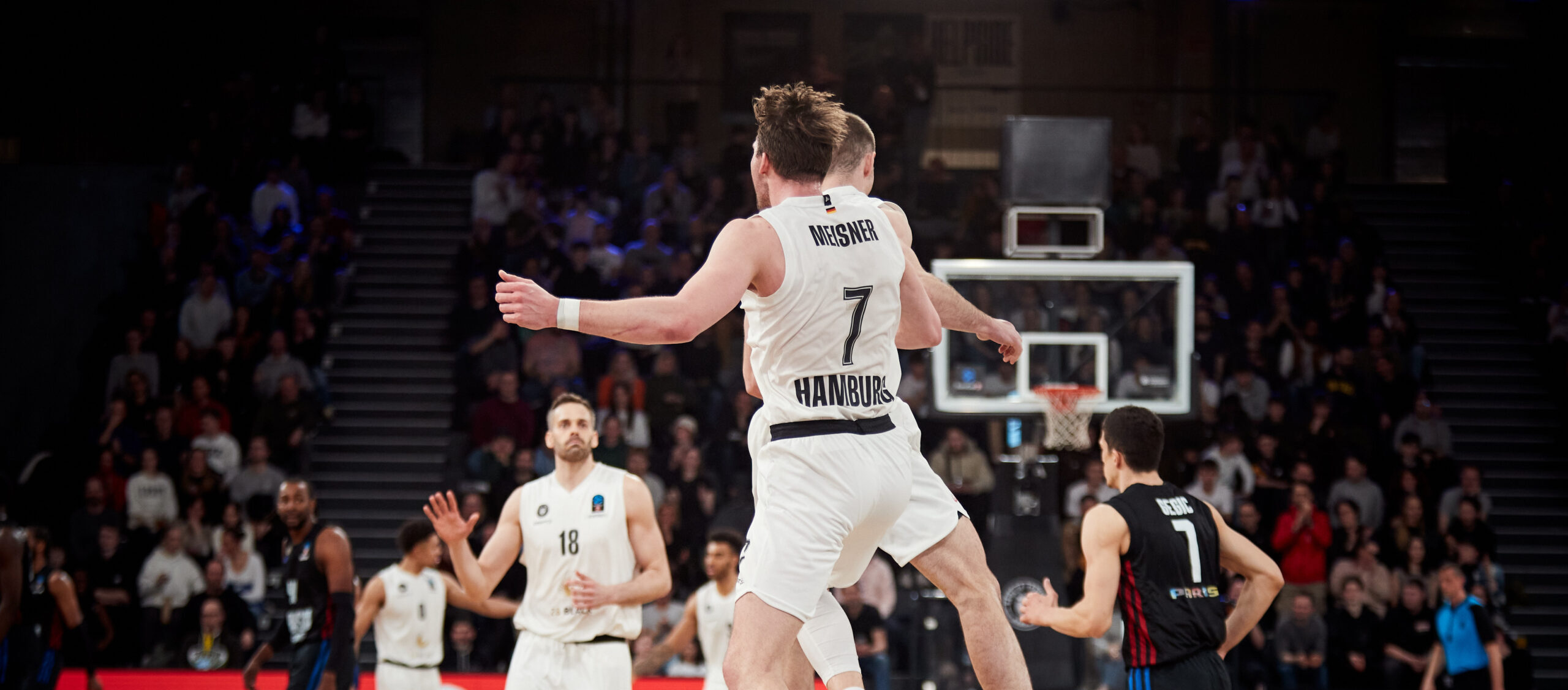 Zwei Basketballspieler der Hamburg Towers in weißen Trikots feiern während eines Spiels gegen Paris, ein Spieler trägt die Nummer 7.