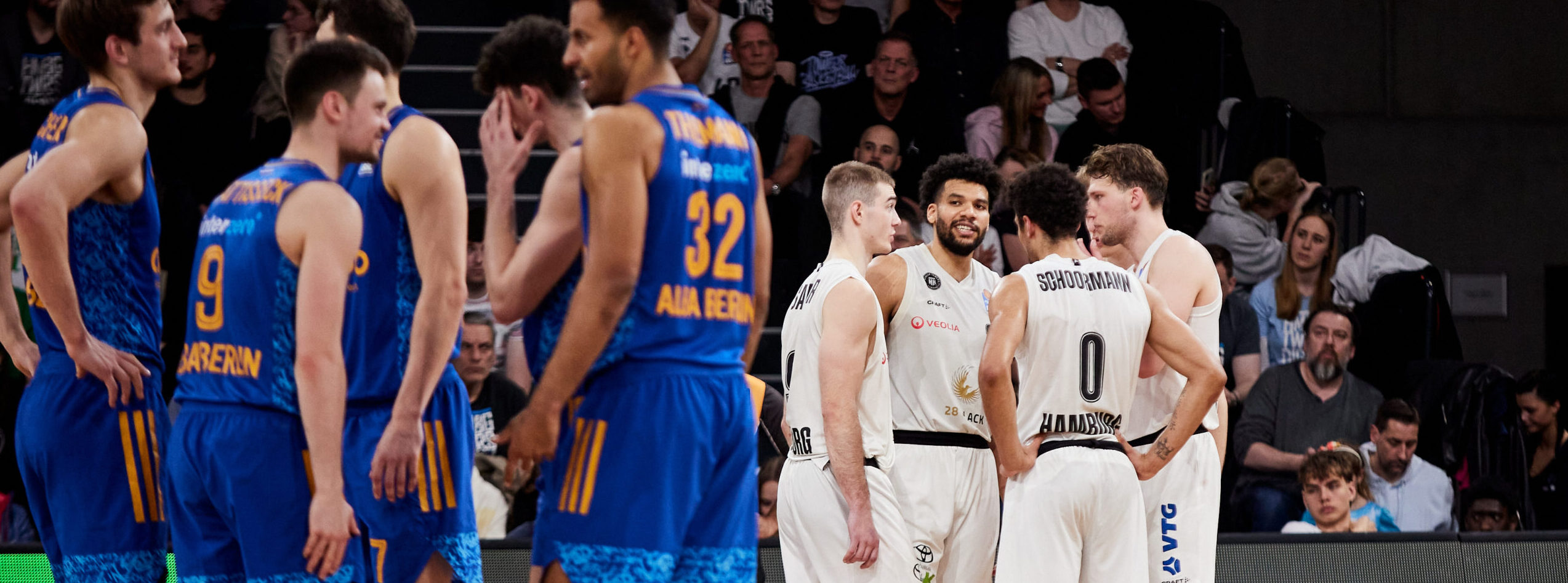 Basketballspieler der Teams Towers Berlin in blauen Trikots und Hamburg in weißen Trikots stehen sich gegenüber während eines Spiels