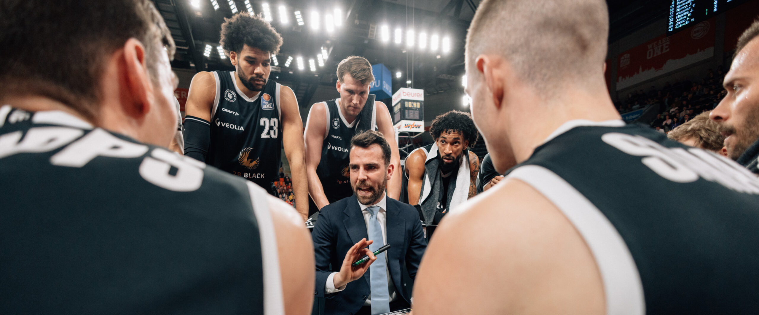 Basketballtrainer spricht mit Spielern während einer Auszeit in einer Halle mit Publikum