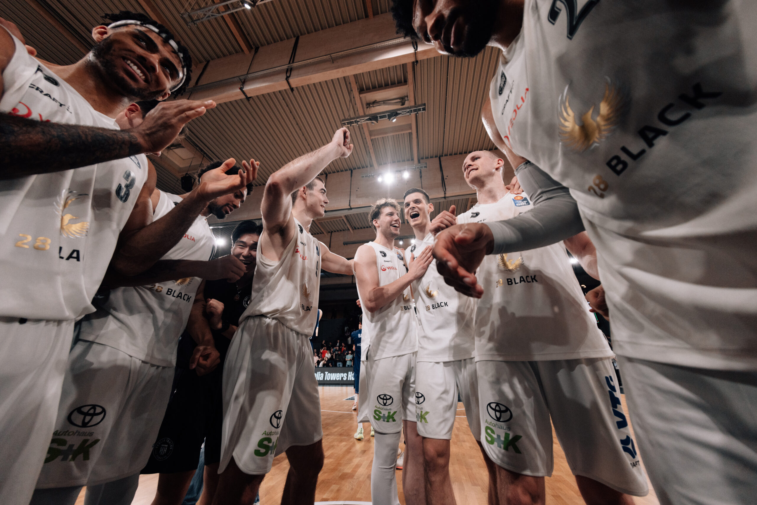 Basketballspieler der Crailsheim Merlins in weißen Trikots klatschen sich vor dem Spiel ab in der Halle
