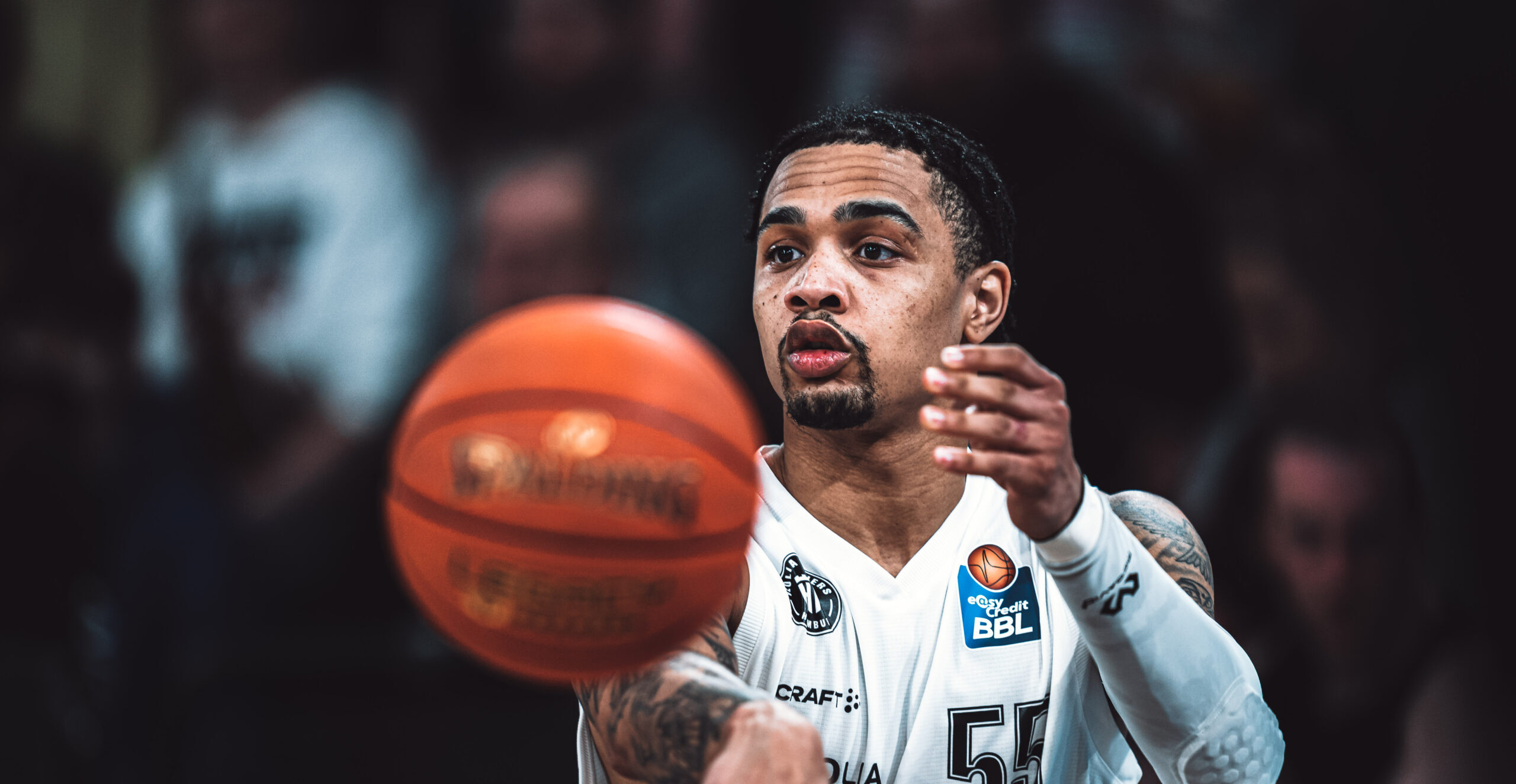 Spieler in weißem Trikot mit "Veolia Towers Hamburg" Logo und Nummer 55 auf der Brust. Er passt den Ball in Richtung der Kamera.