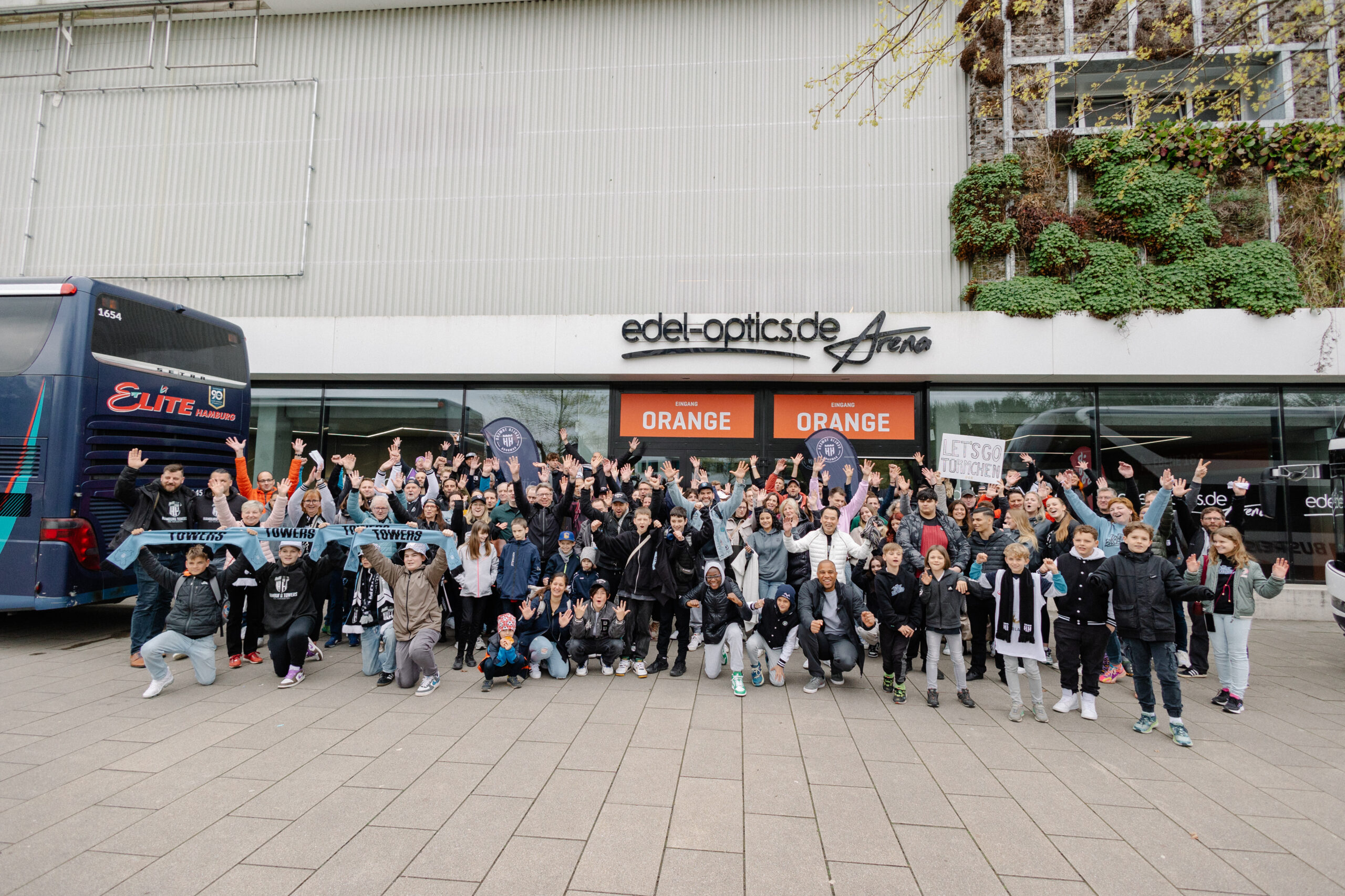 Große Gruppe von Menschen vor der Arena 'edel-optics.de Arena', viele heben die Arme und halten Schilder mit 'LET'S GO Towers'