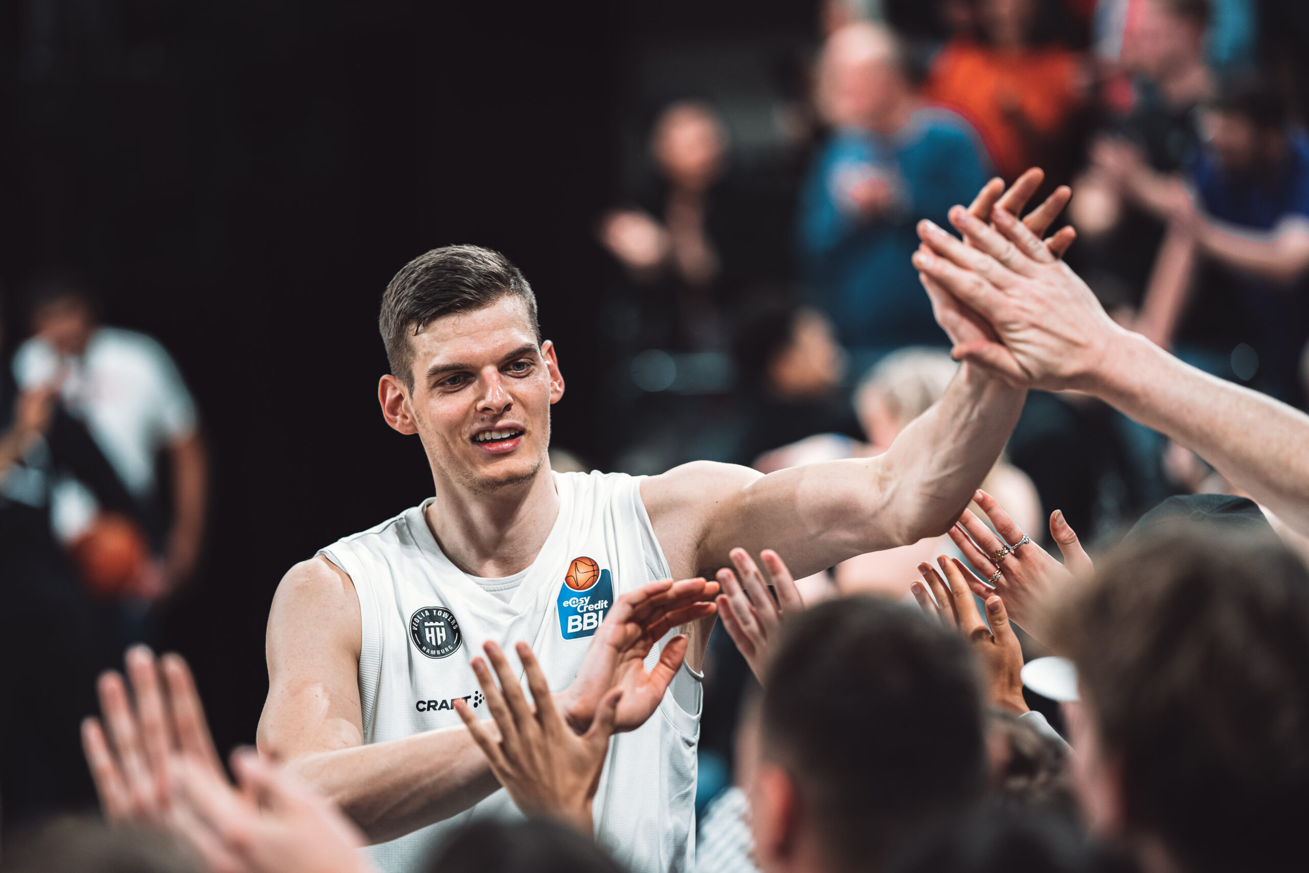 Basketballspieler in weißem Trikot gibt Fans nach Spiel High-Fives, Menschenmenge im Hintergrund