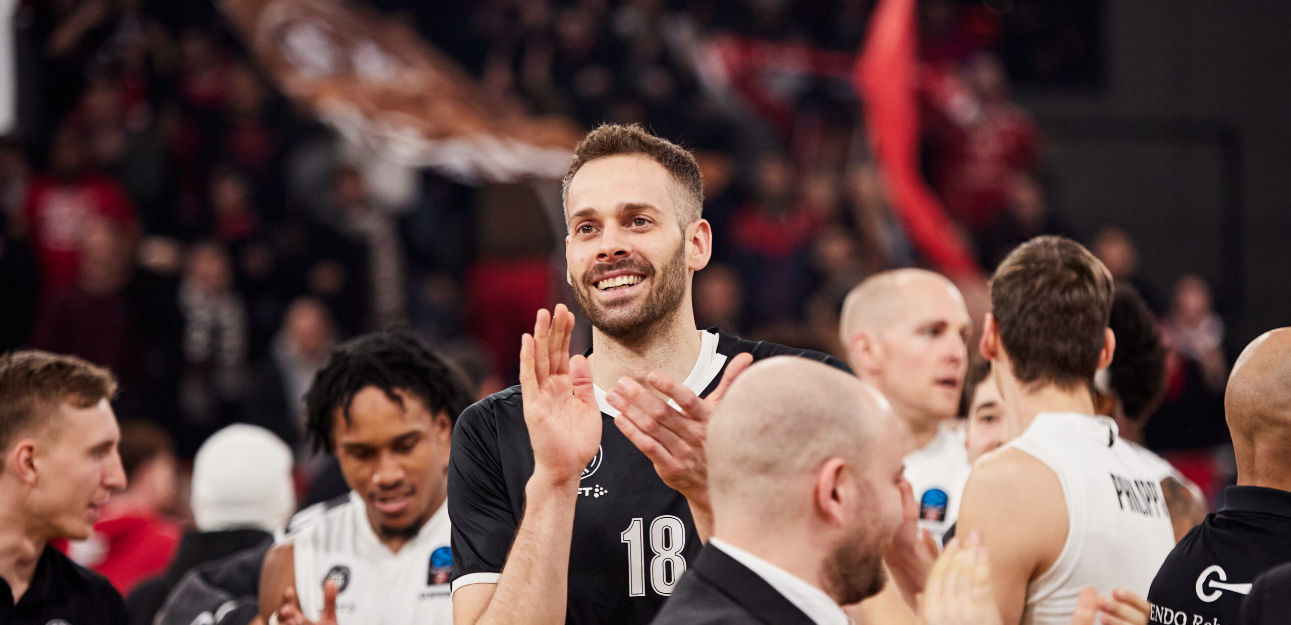 Basketballspieler in schwarzen Trikots klatschen während eines Spiels, umgeben von Teamkollegen und Publikum