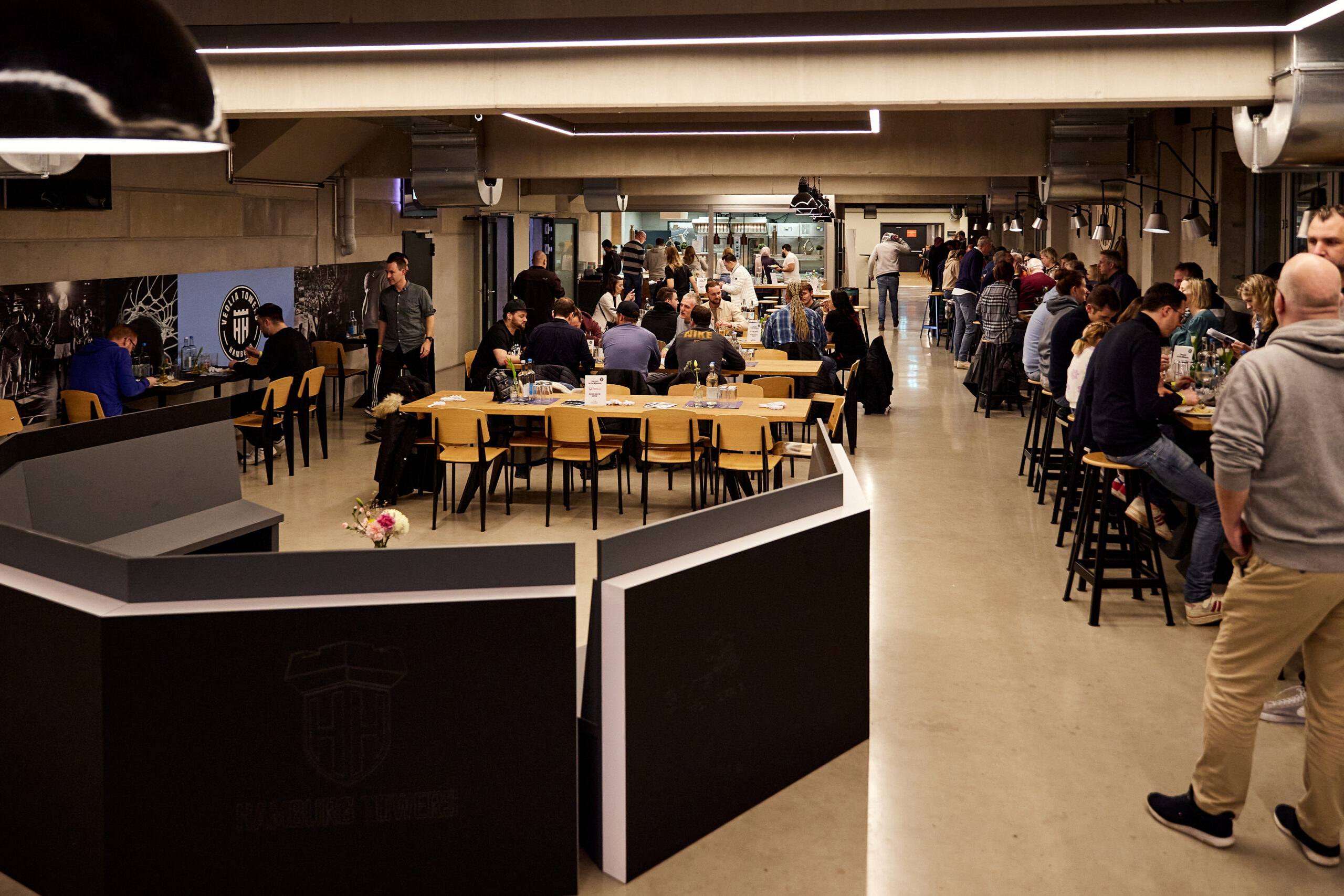 Innenraum eines Cafés mit mehreren Tischen und Stühlen, viele Menschen sitzen und unterhalten sich