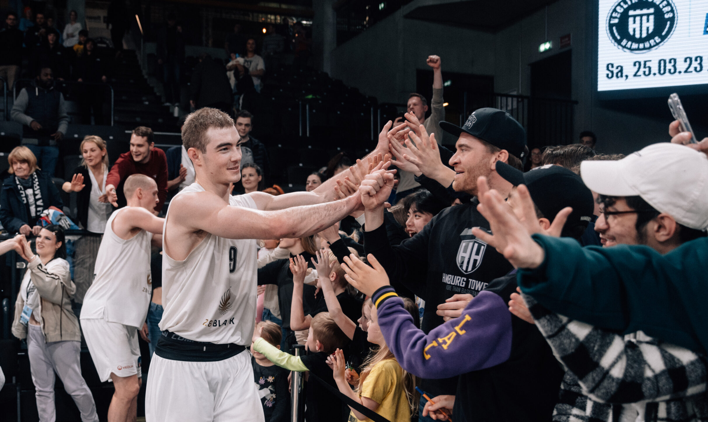 Basketballspieler in weißem Trikot mit der Nummer 9 gibt Fans nach Spiel High-Fives in Halle