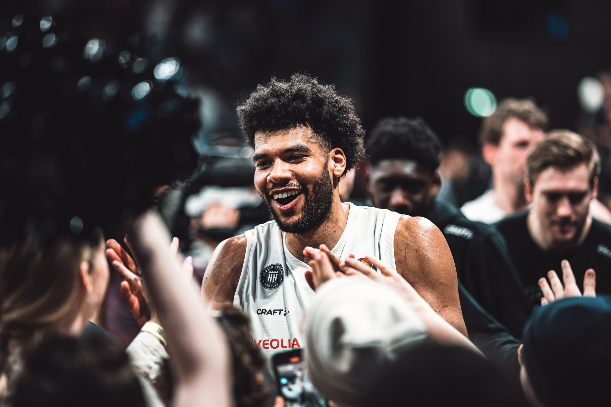 Basketballspieler in weißem Trikot klatscht bei Fans ab