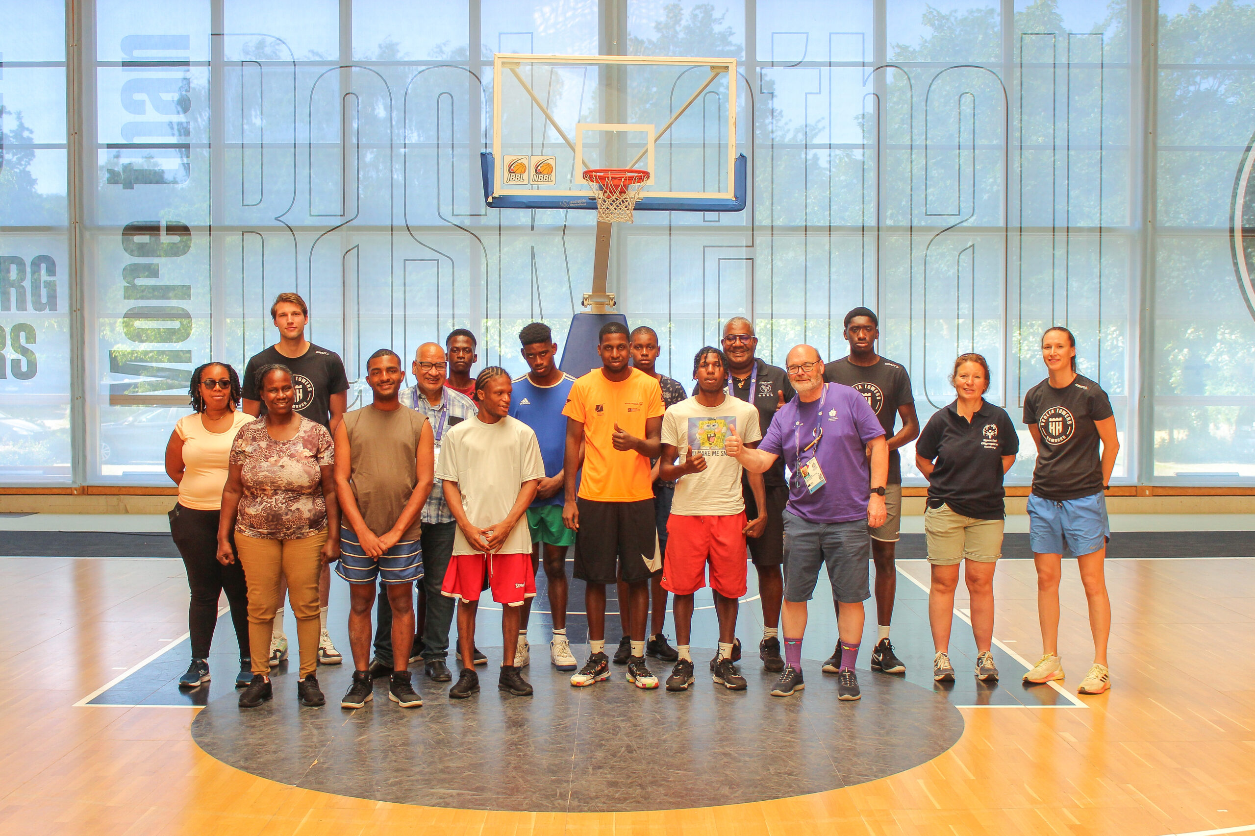 Gruppe von 15 Personen steht in einer Sporthalle vor einem Basketballkorb auf dem Spielfeld