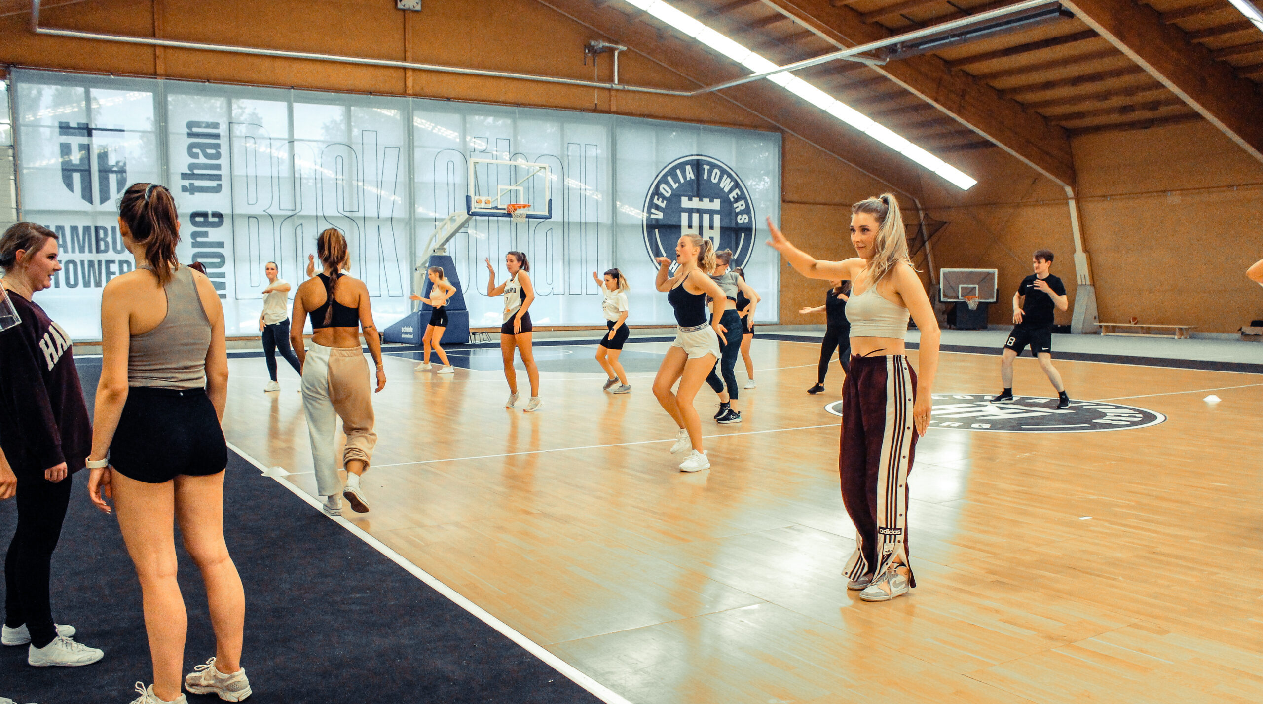 Junge Frauen tanzen in Sportkleidung in einer Turnhalle mit großem Veolia Towers-Logo an der Wand