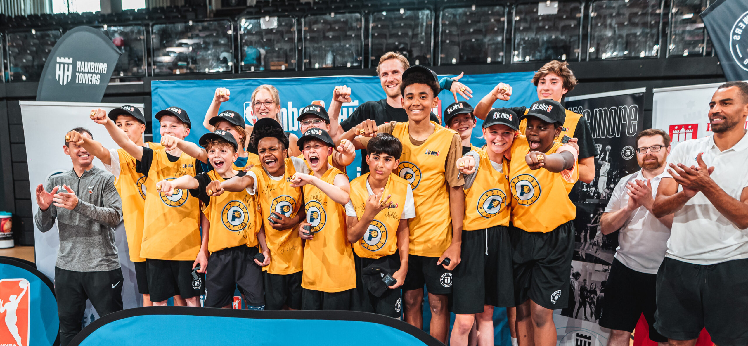Jugendbasketballteam Hamburg Towers in gelben Trikots posiert mit erhobenen Fäusten in einer Halle während der JR NBA Finals 2023