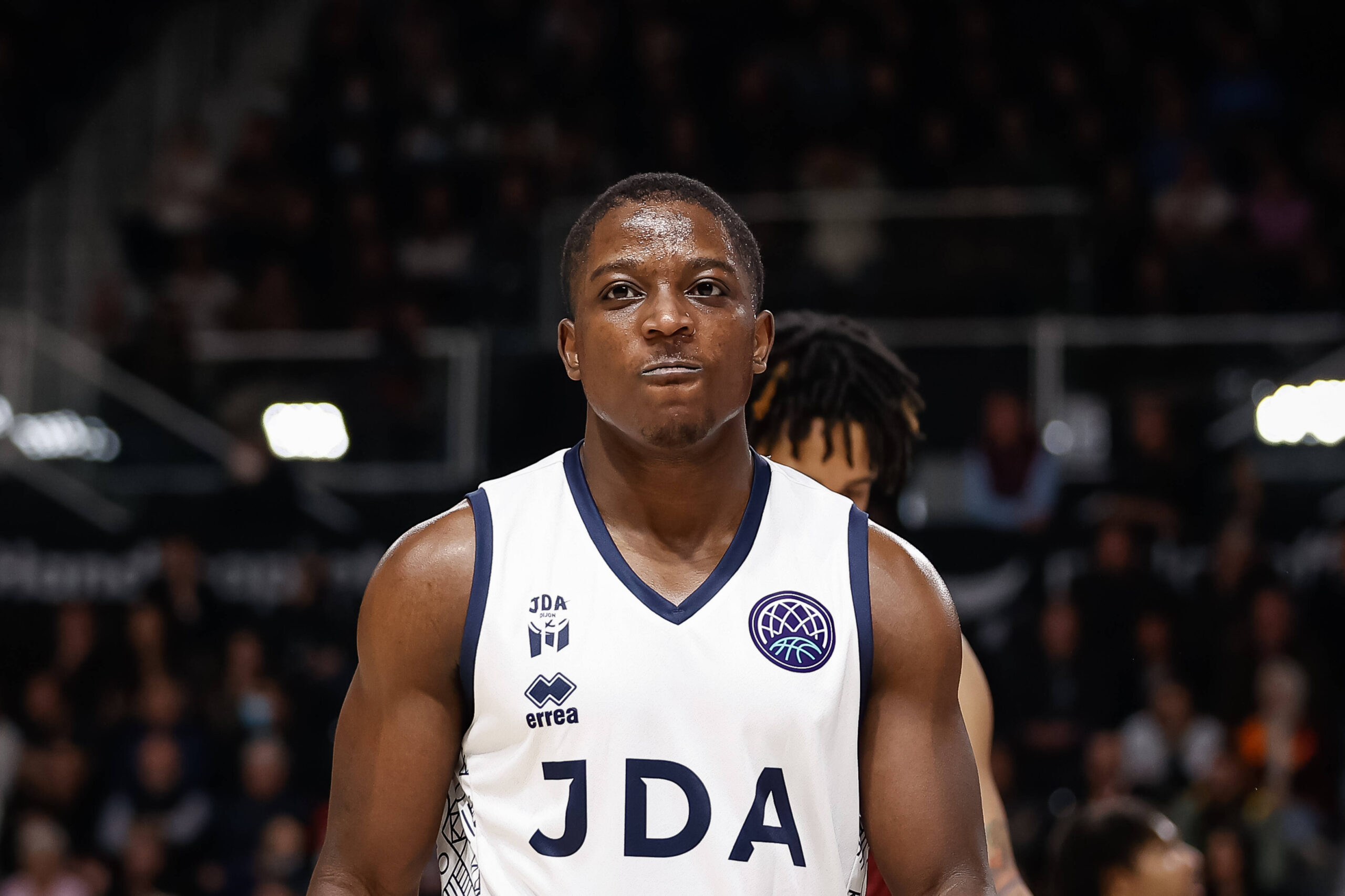 Basketballspieler in rotem Trikot mit der Aufschrift 'GIESSEN' steht neben einem Schiedsrichter in grauem Hemd während eines Spiels