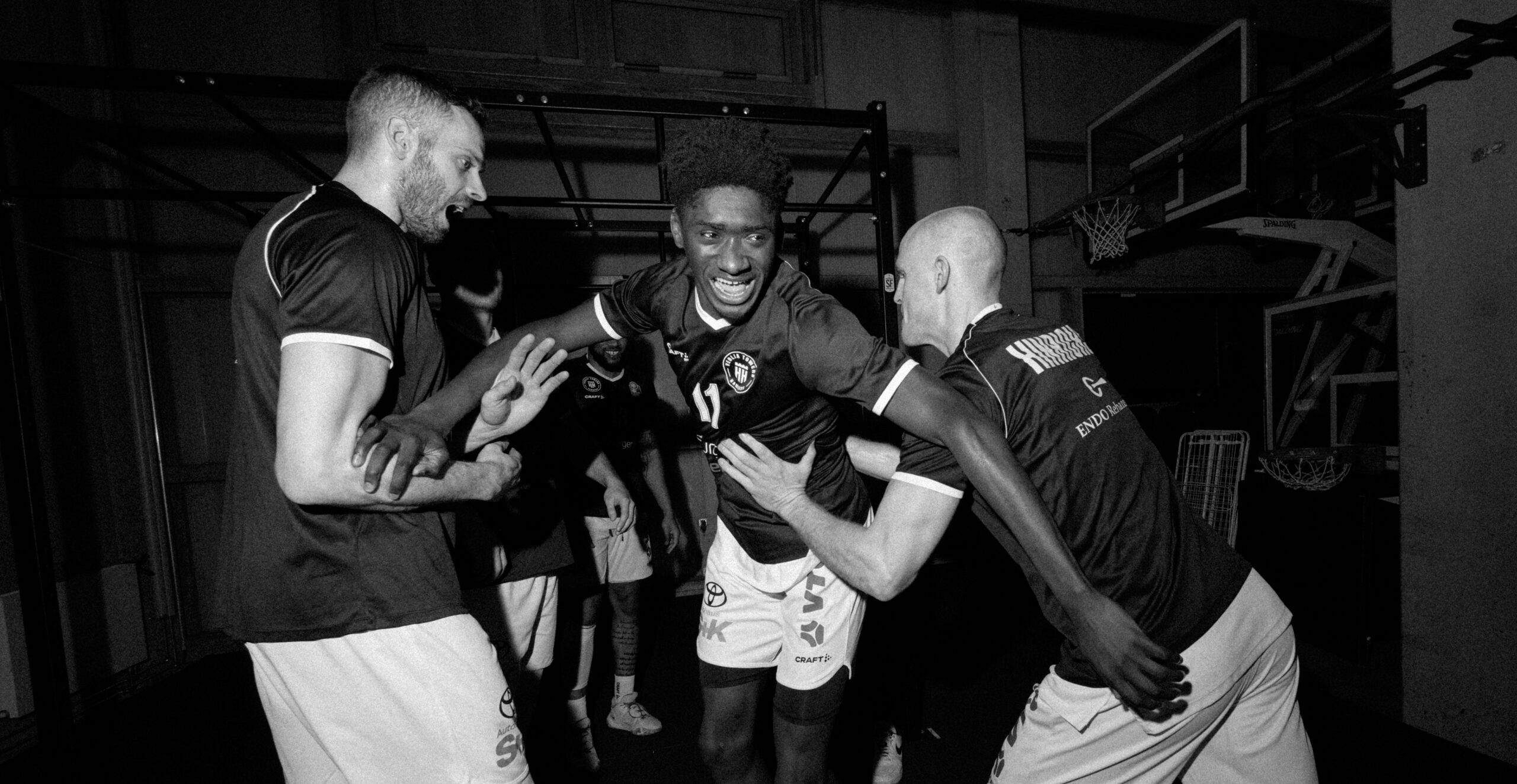 Drei Basketballspieler in Trikots umarmen sich und feiern in einer Halle