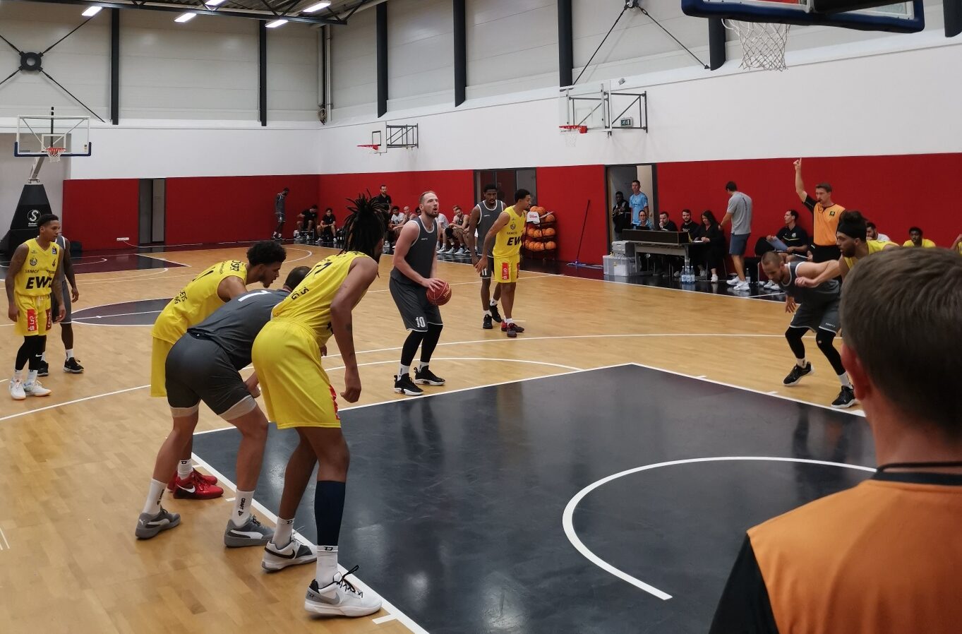 Basketballspiel in Halle mit Spielern in gelben und schwarzen Trikots, ein Spieler bereitet sich auf Freiwurf vor
