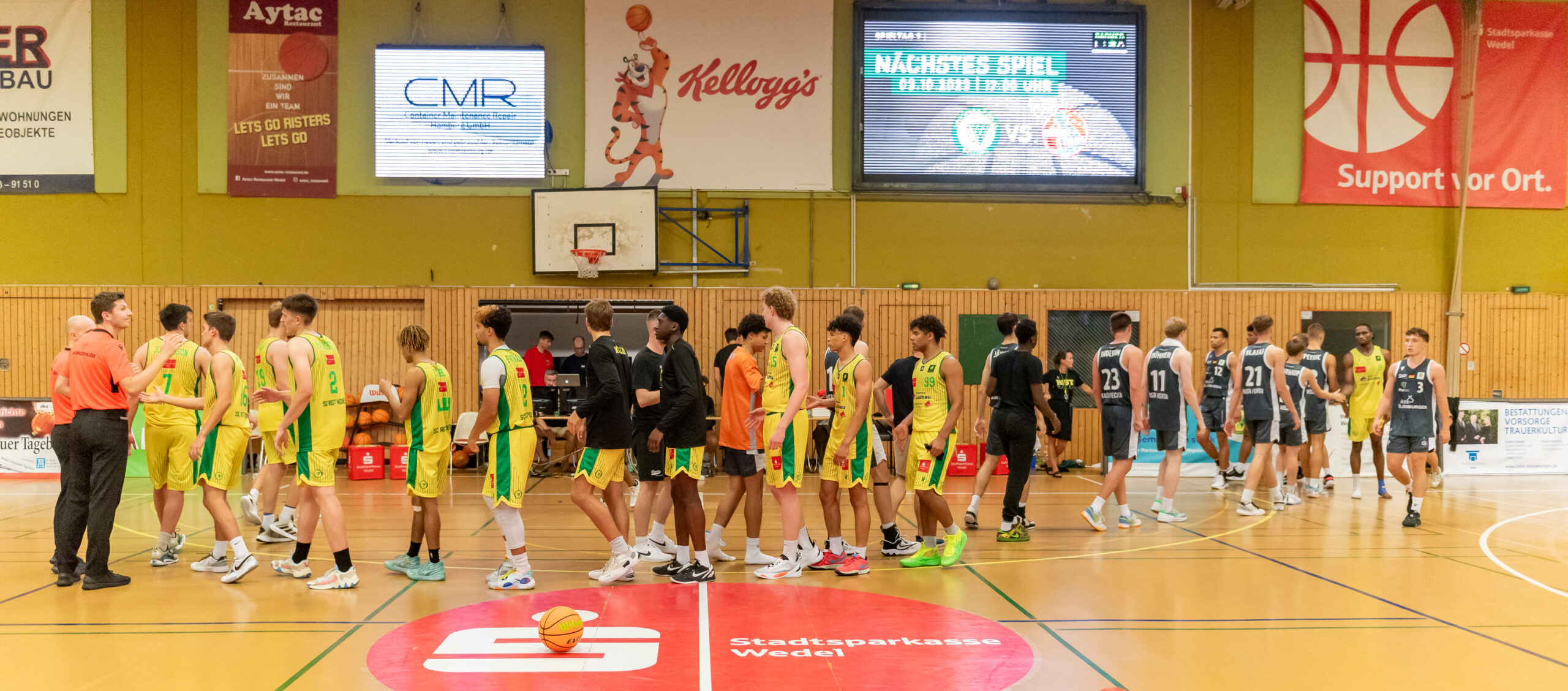 Basketballspieler in gelben und schwarzen Trikots geben sich nach dem Spiel in einer Halle die Hand